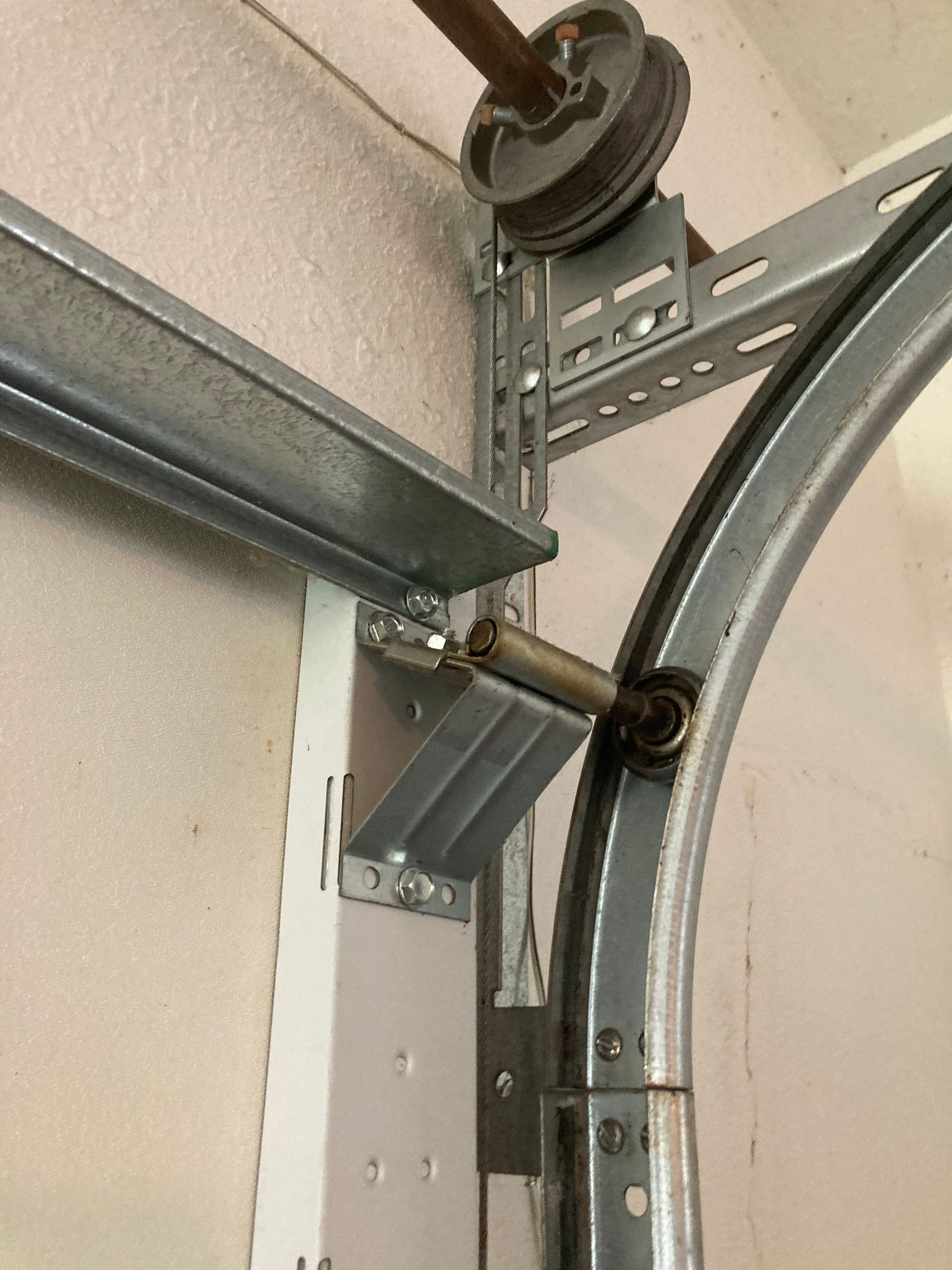 Garage door track and hardware close-up with a curved metal rail and pulley assembly.