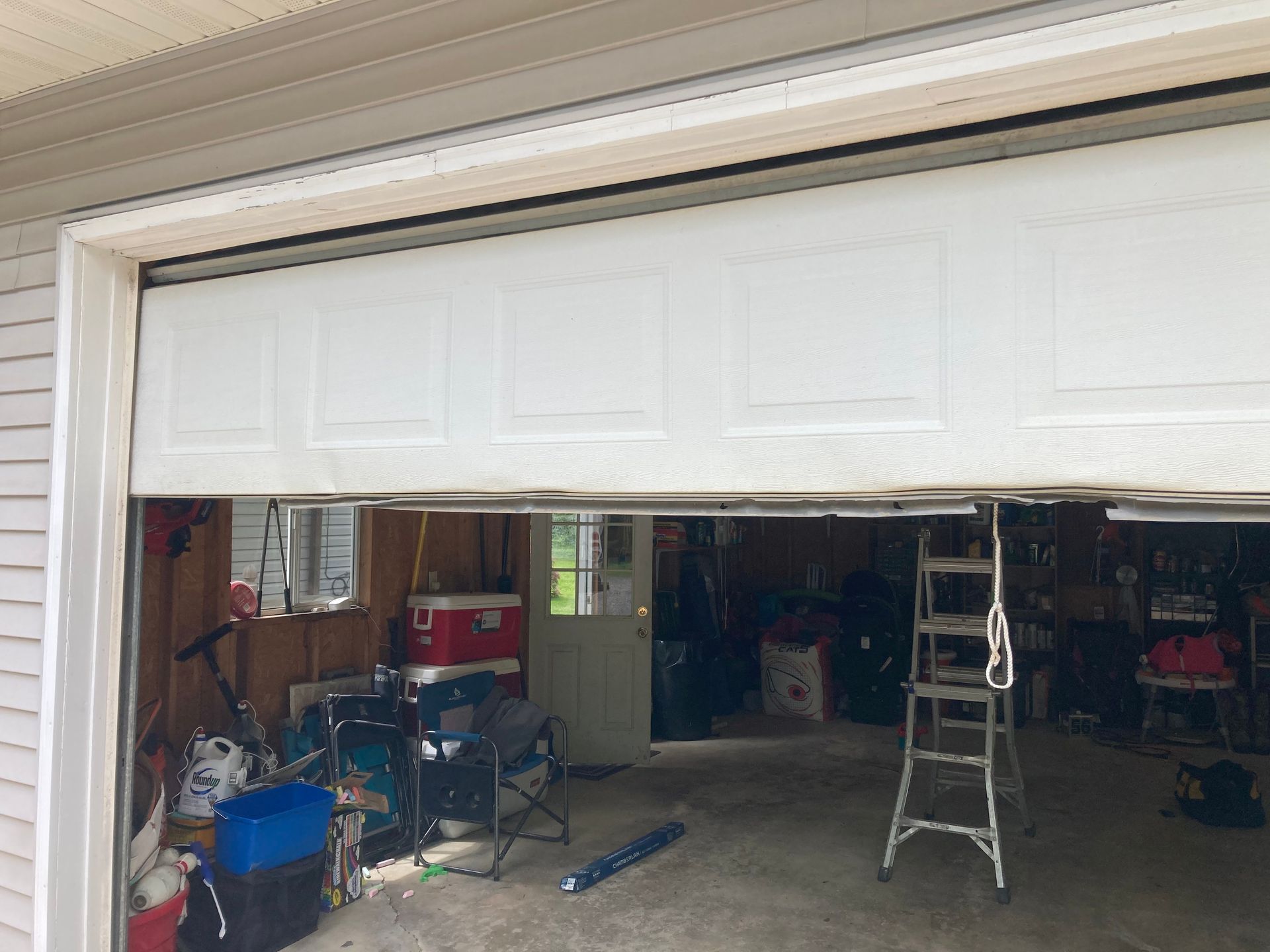 Partially open garage door with a step ladder and cluttered tools inside