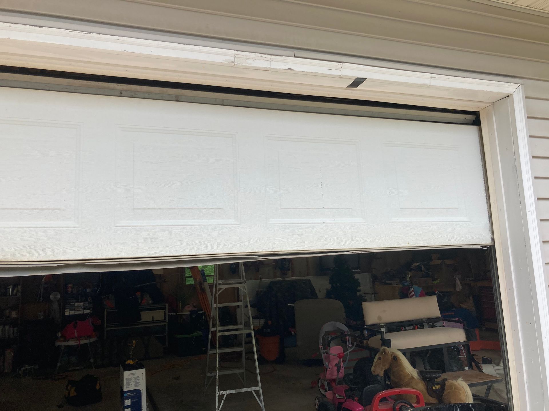 Partially open garage door revealing a cluttered garage with a ladder and stored items inside