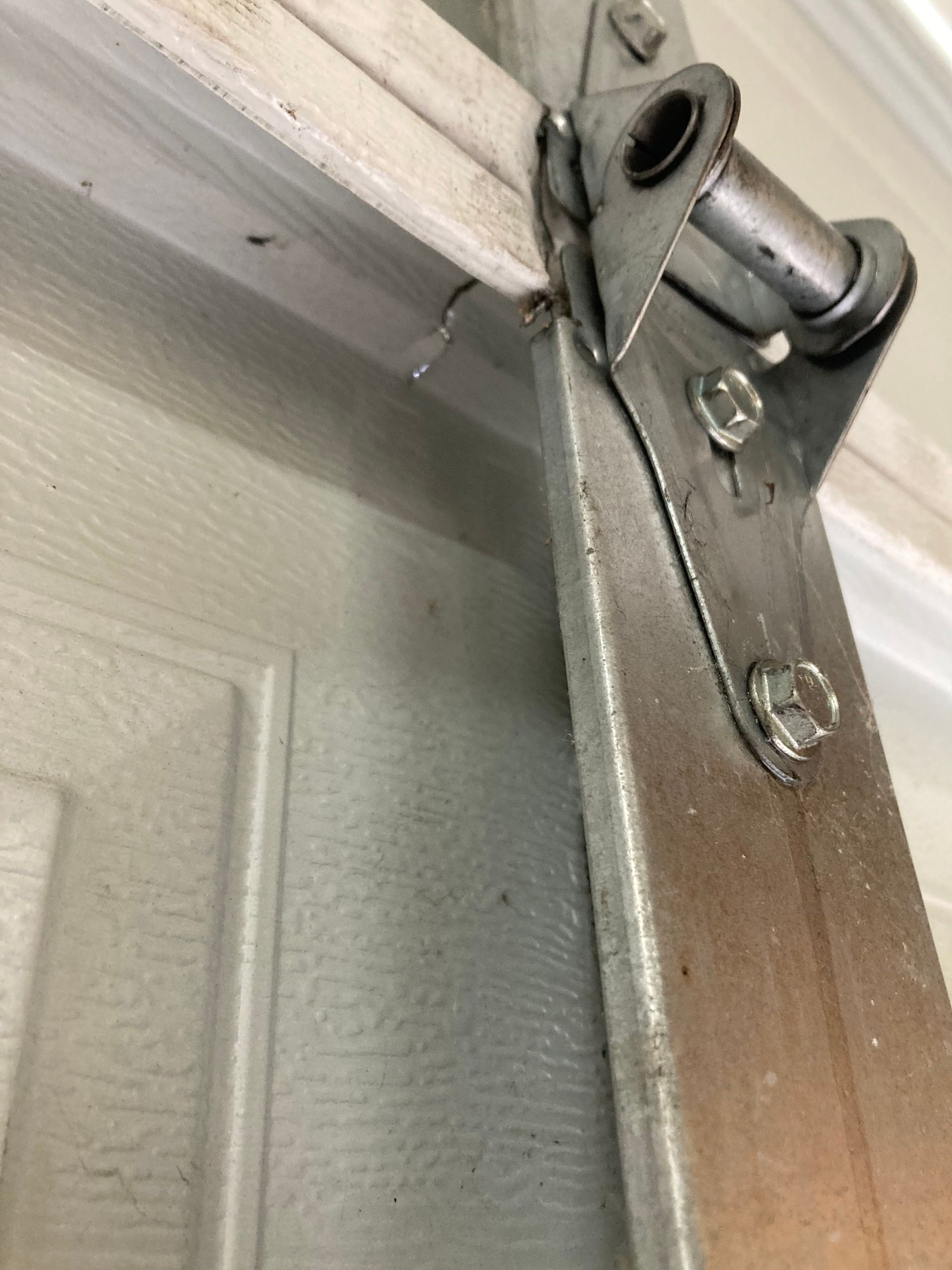 Close-up of a metal garage door hinge mounted near the top of a painted door.