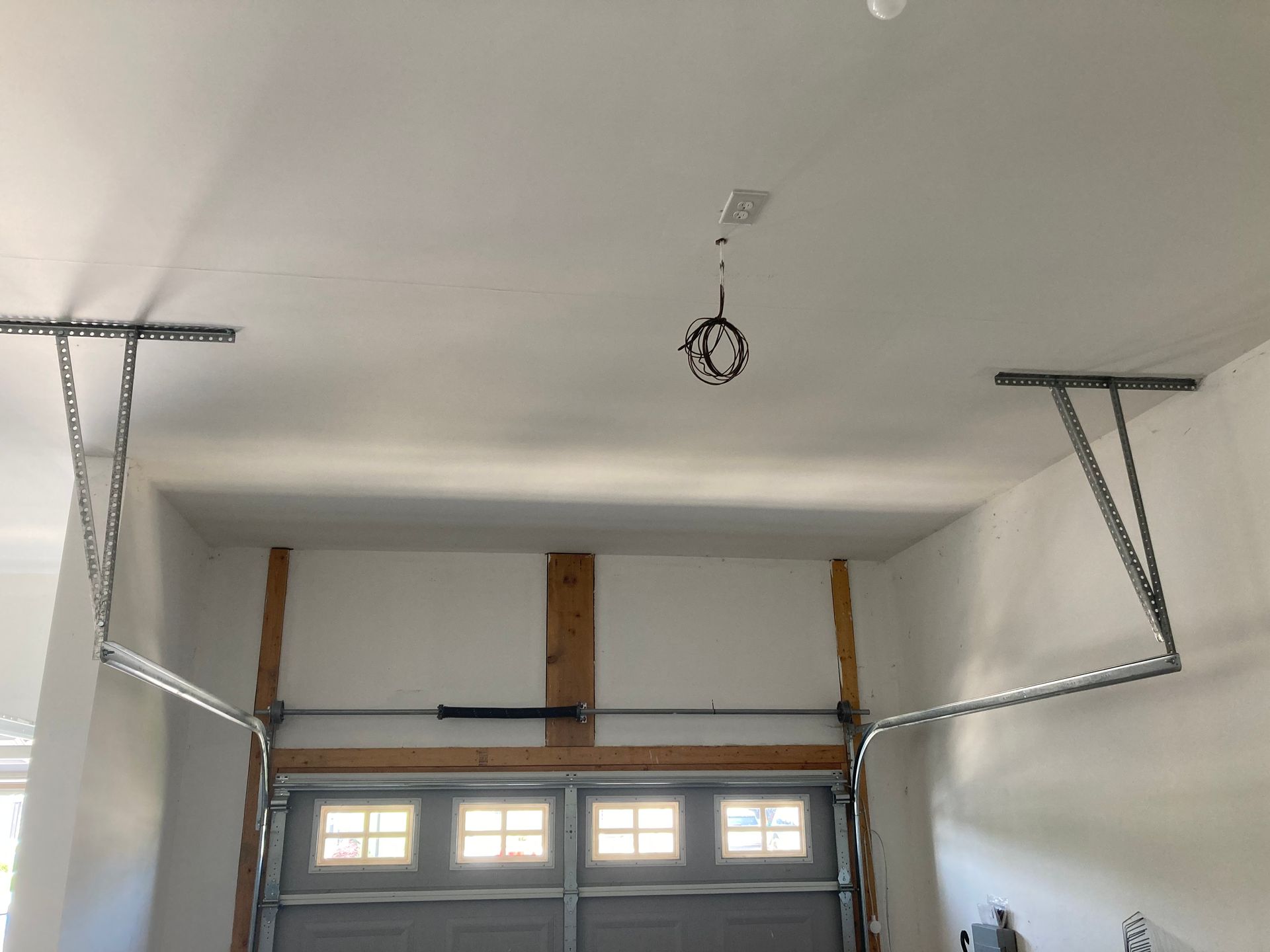 Garage interior with unfinished drywall, ceiling hooks, and the garage door opening below