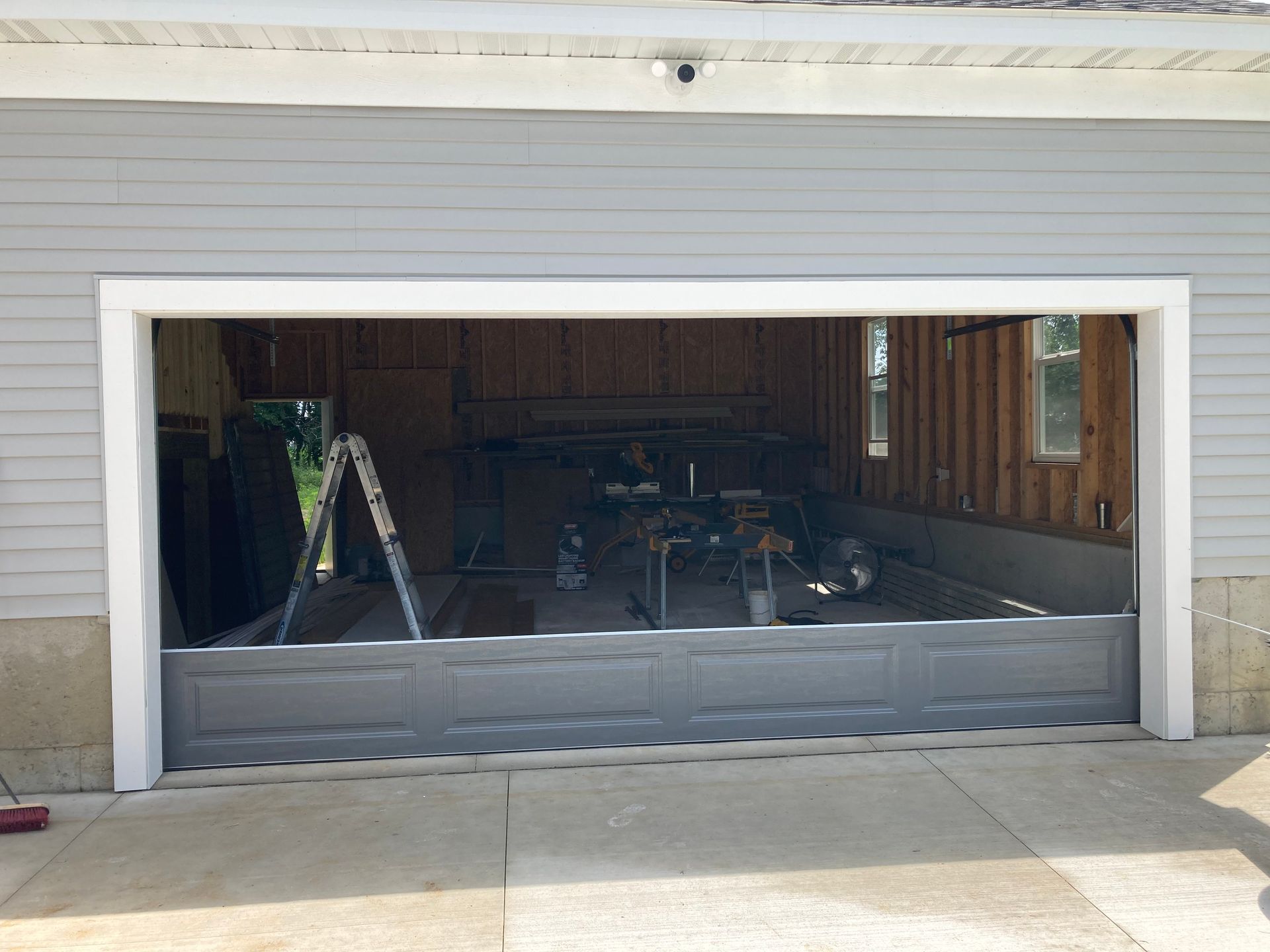 Open garage with a ladder and tools visible inside, gray door partially raised.