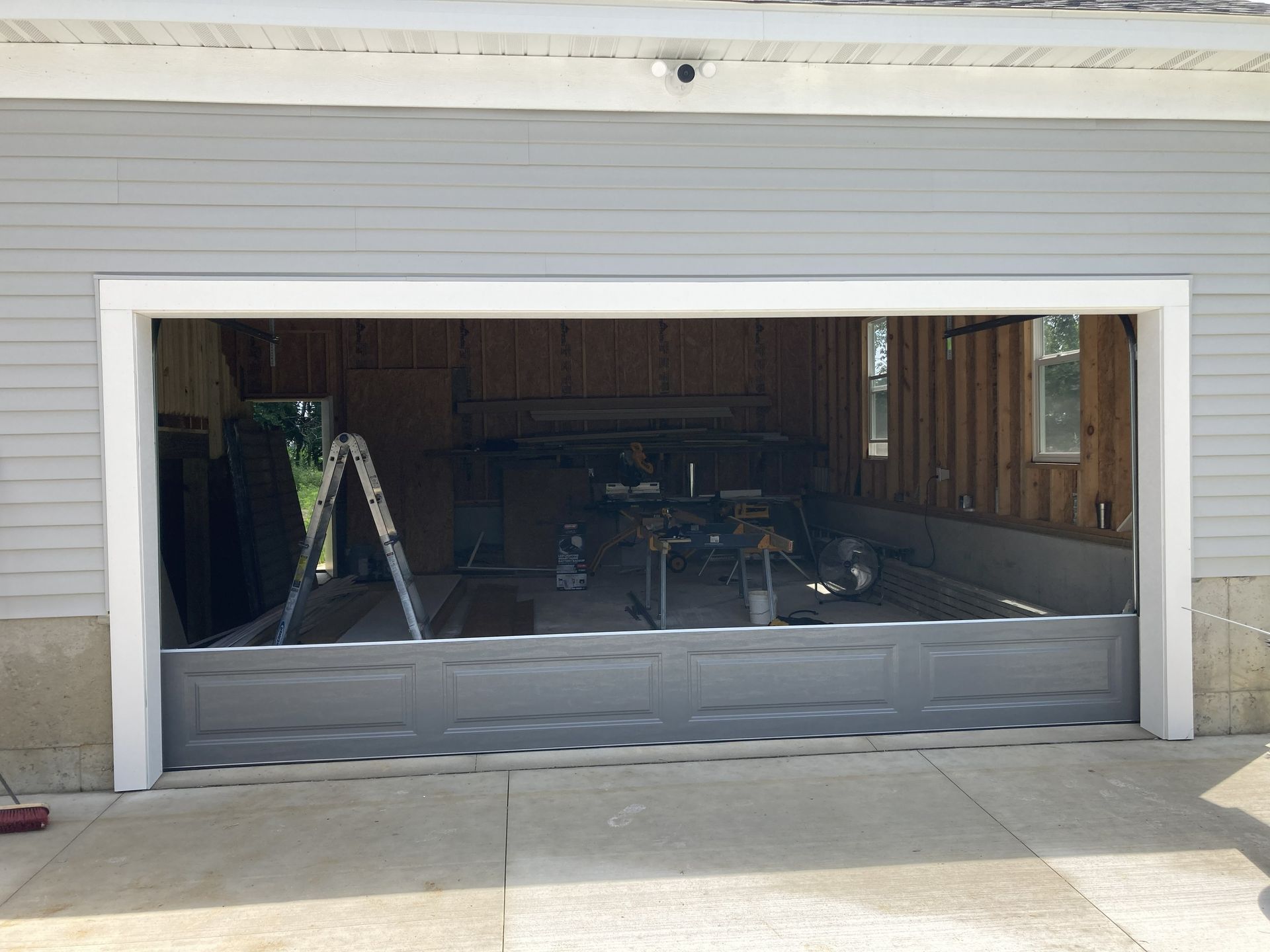 Open garage with black gate, showing a workshop inside and a ladder on the left.