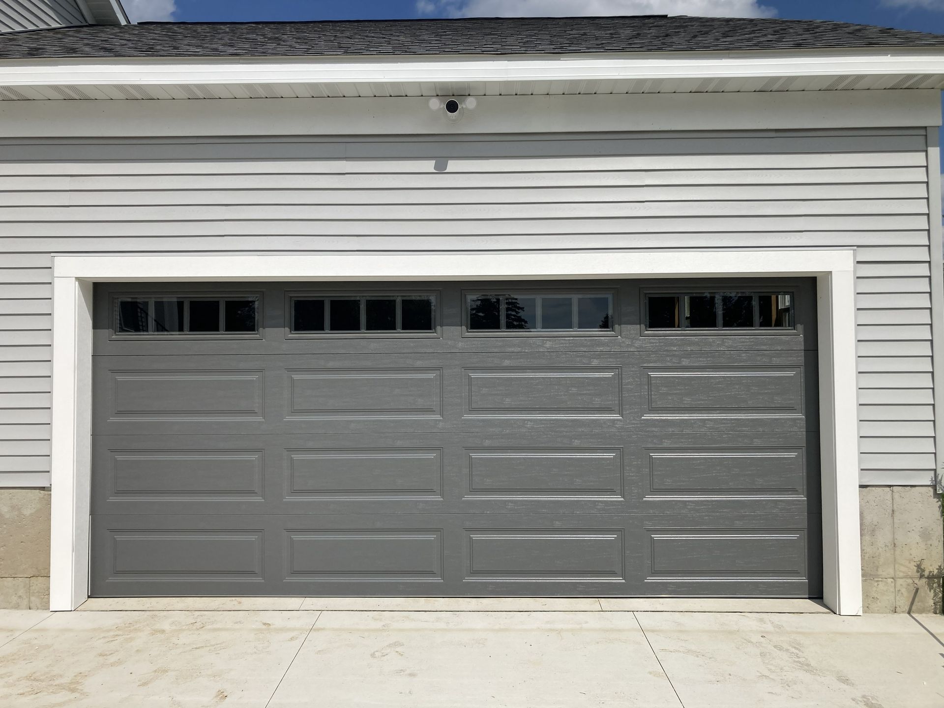 Closed gray garage door with small windows in a white-sided house exterior