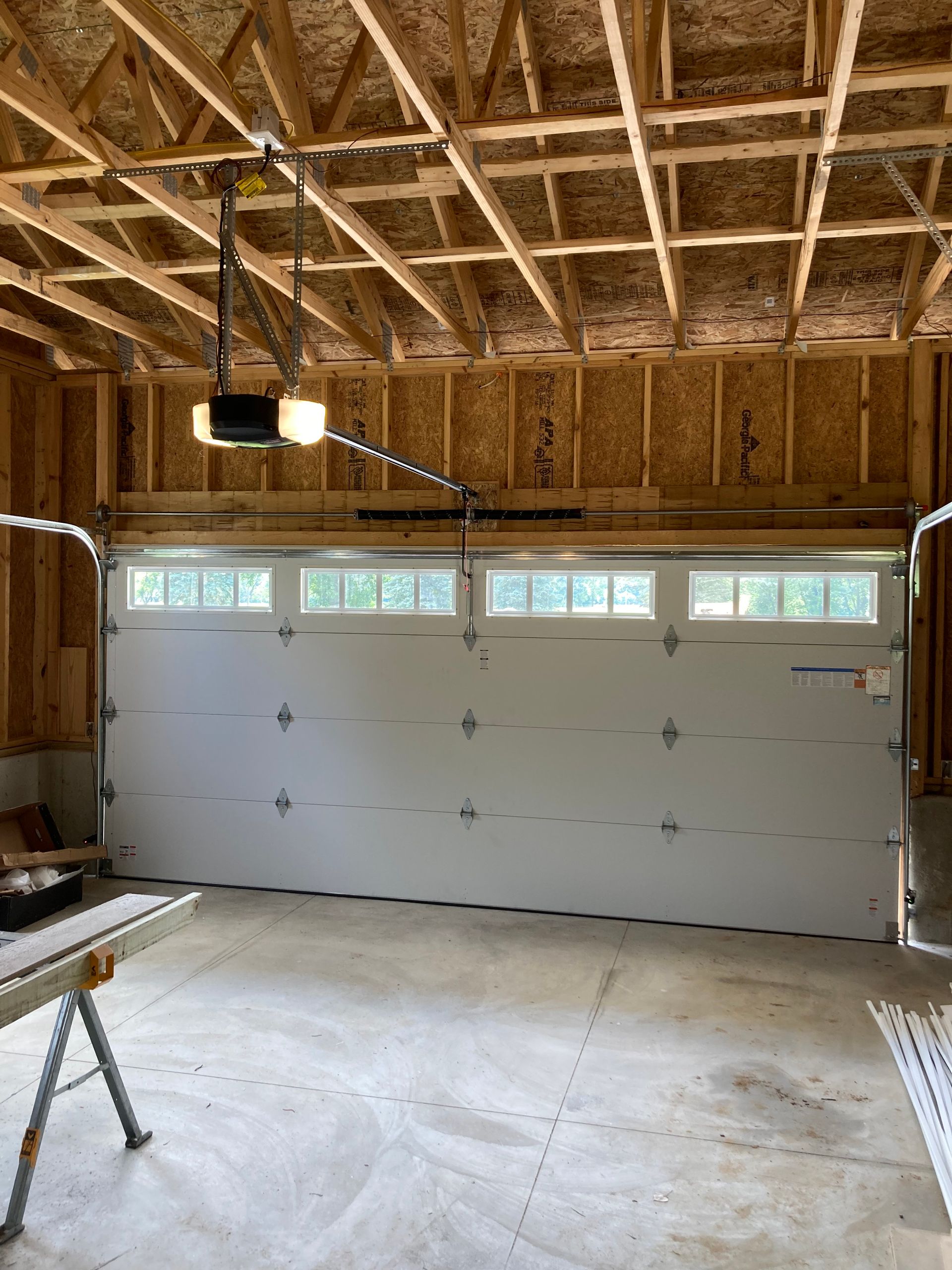 Unfinished garage interior with a white sectional door and exposed wooden framing ceiling.