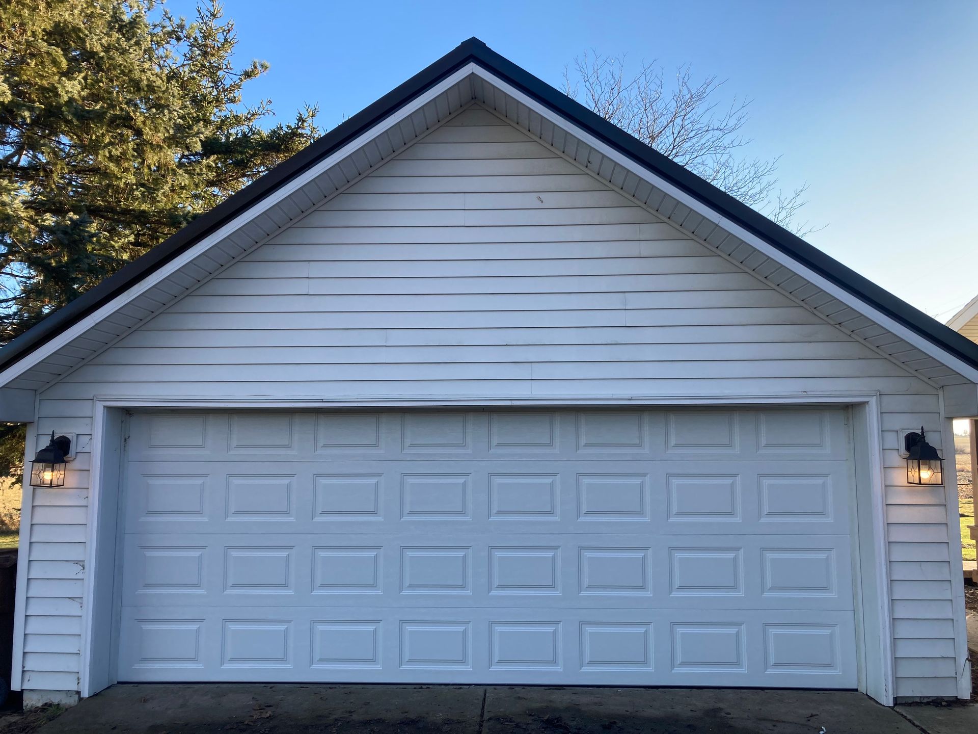 White detached garage with a two-car door and gabled roof at dusk