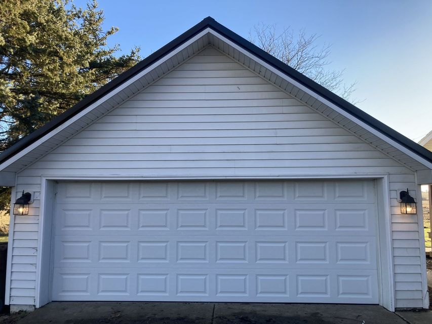 White double garage door on a detached house with light siding and gabled roof at dusk