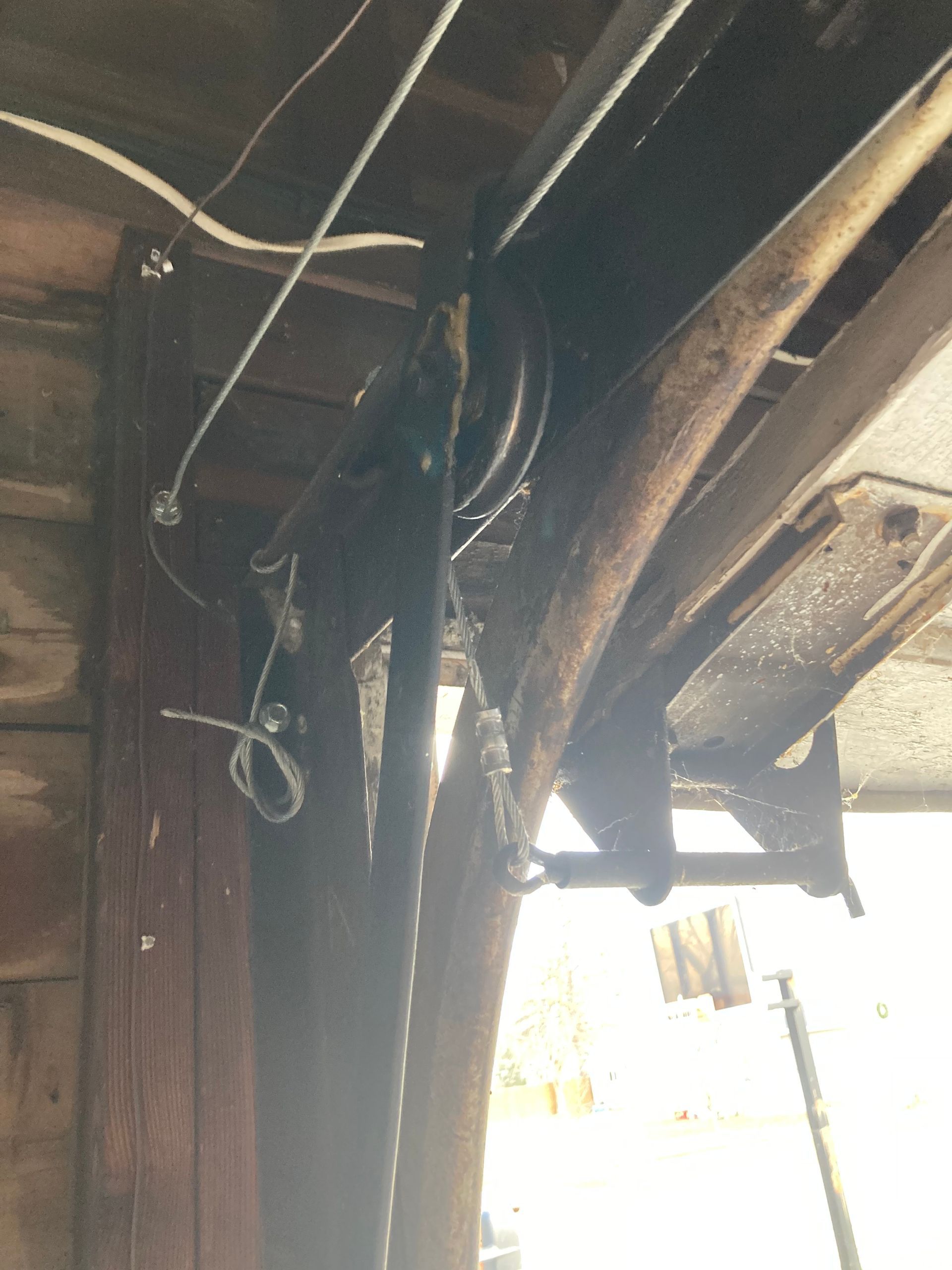 Damaged ceiling with exposed wooden beams, hanging wires, and bright daylight from an opening below