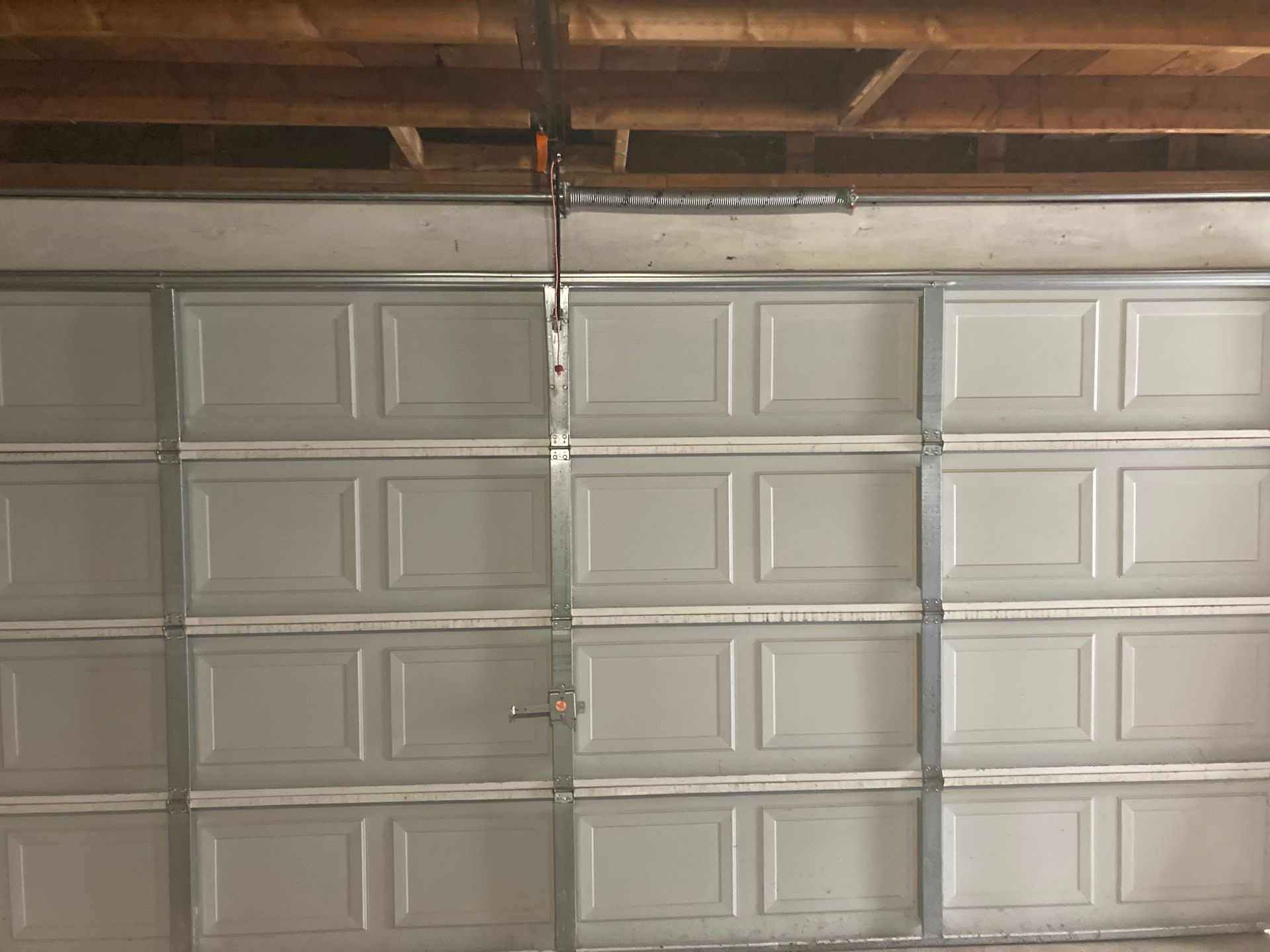 Closed white garage door with a center seam in a wood-framed garage interior