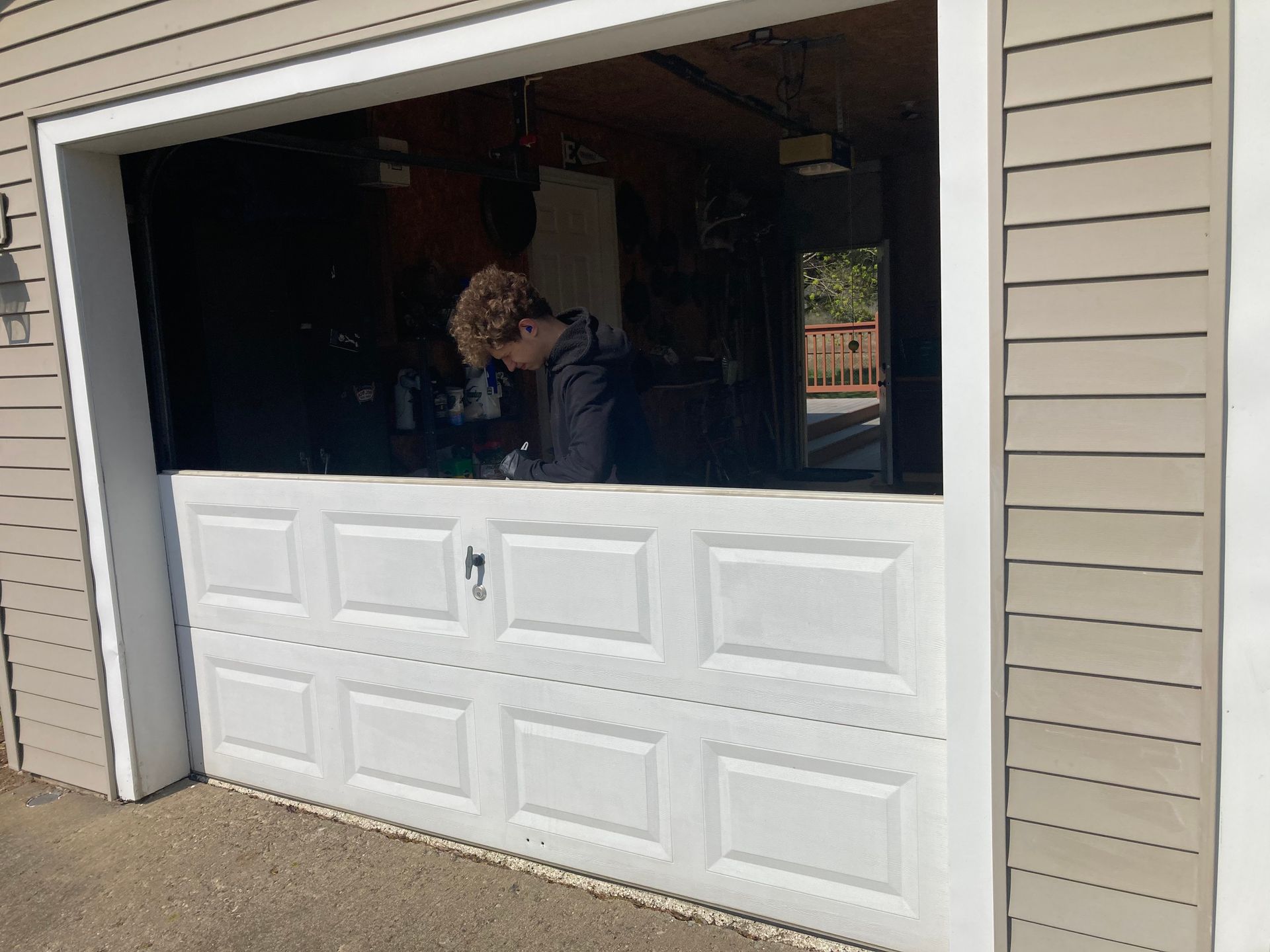 Half-open garage door with a person inside, white door panel below and beige siding around it