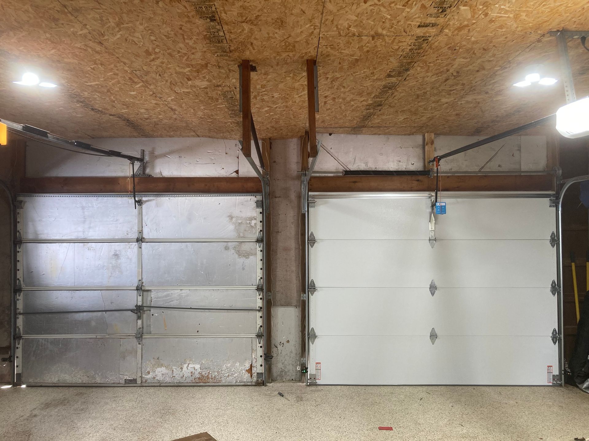 Garage interior with three closed doors, concrete floor, and a wood-paneled ceiling.