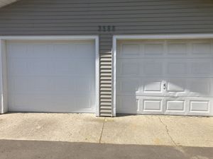 Two white garage doors on a house exterior with beige siding and a concrete driveway.