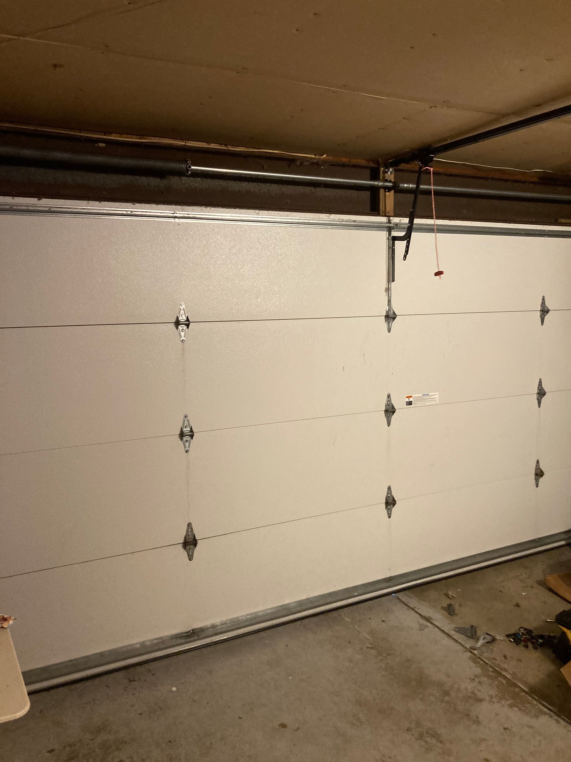Closed white garage door with black hardware in a concrete garage, viewed from inside.