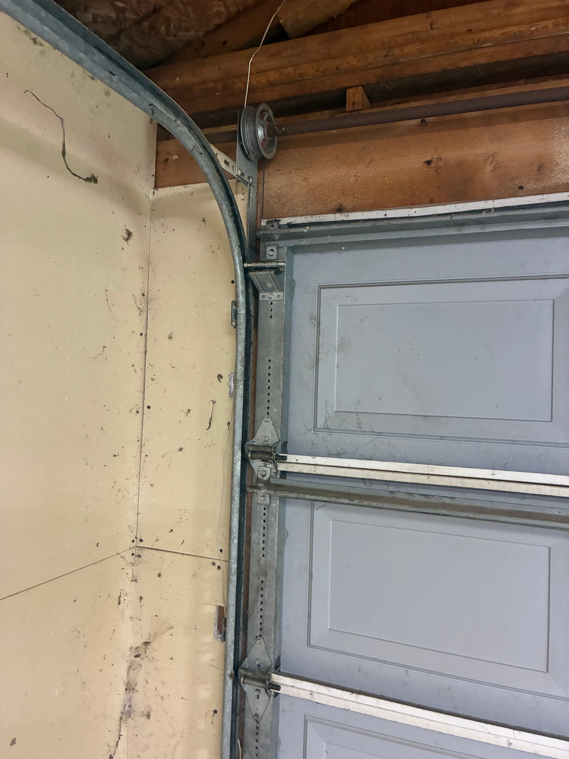 Interior garage corner with a gray overhead door track and exposed wood framing above.