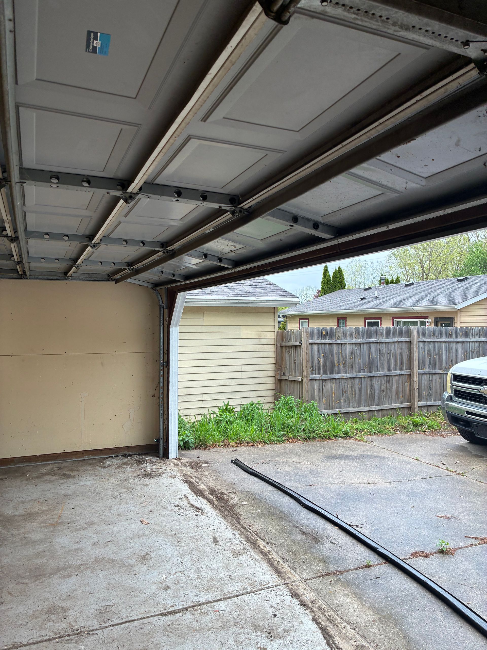 Open garage interior with concrete floor, driveway outside, wooden fence, and front of a parked vehicle