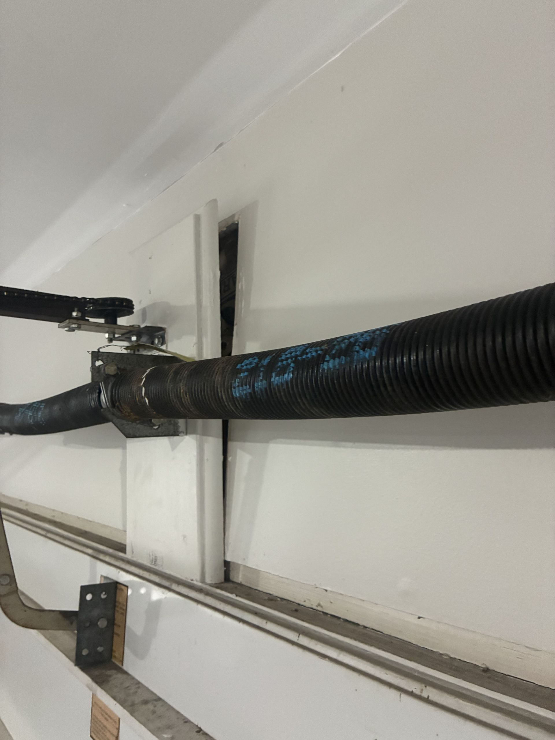 Black ribbed hose and cables secured along a white wall inside a utility space.