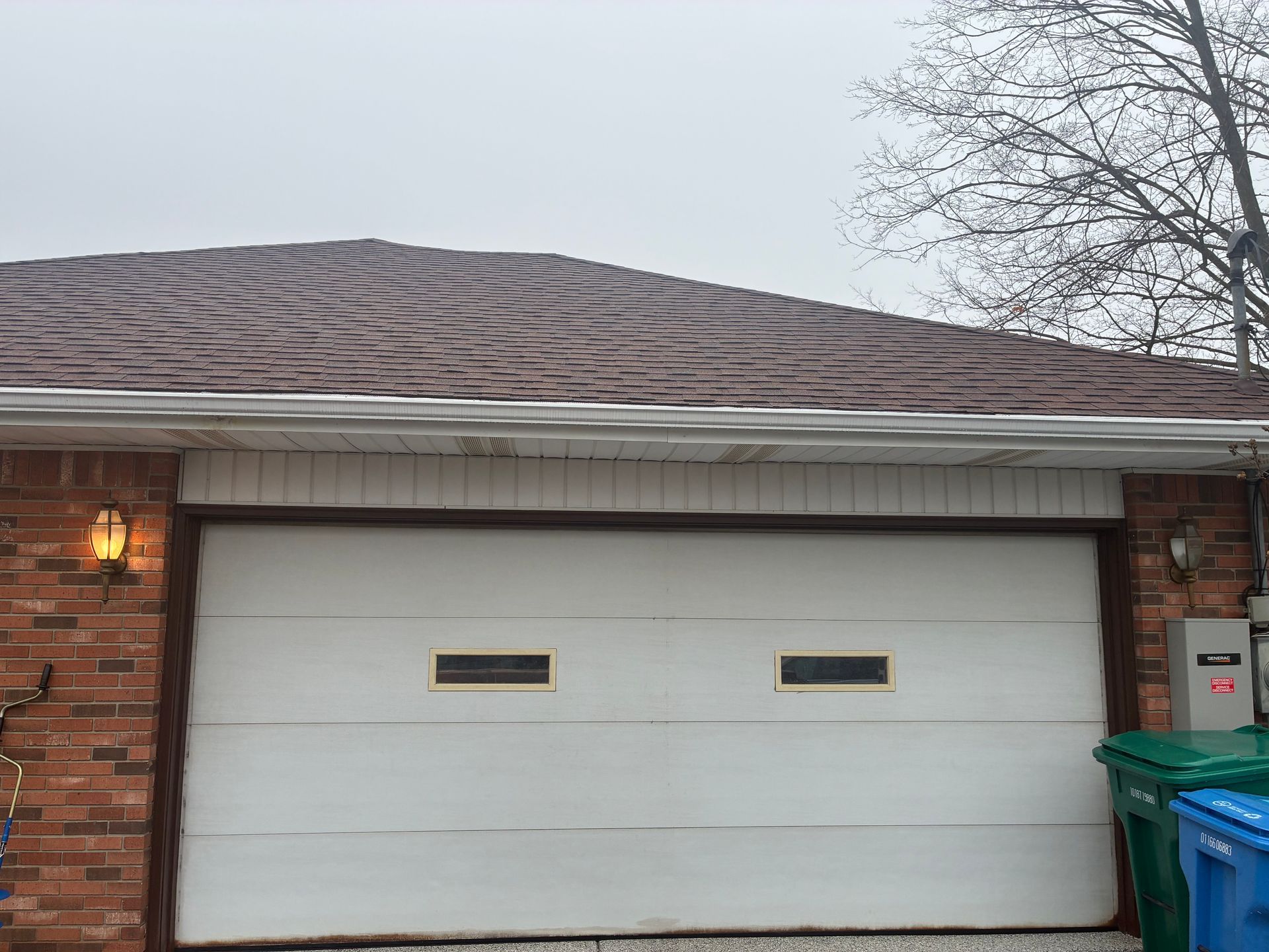 Single-car garage with white door, red brick exterior, and a dumpster at the right side.