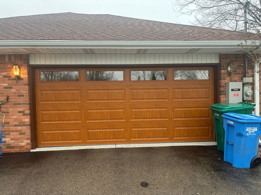 Residential garage with a wood-paneled door and two trash bins on the right.