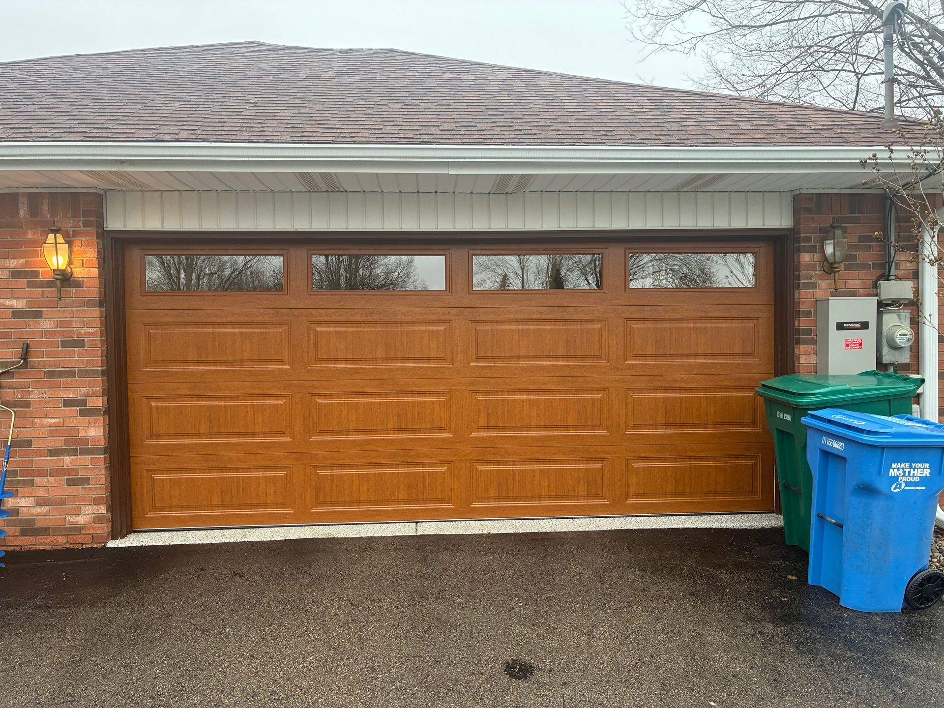 Brick house garage with a brown door and blue trash bins on a wet driveway