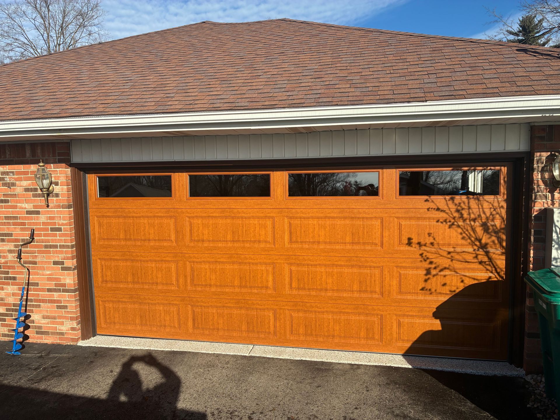 Orange garage door beneath a white-trimmed roof on a brick house, viewed from the driveway.