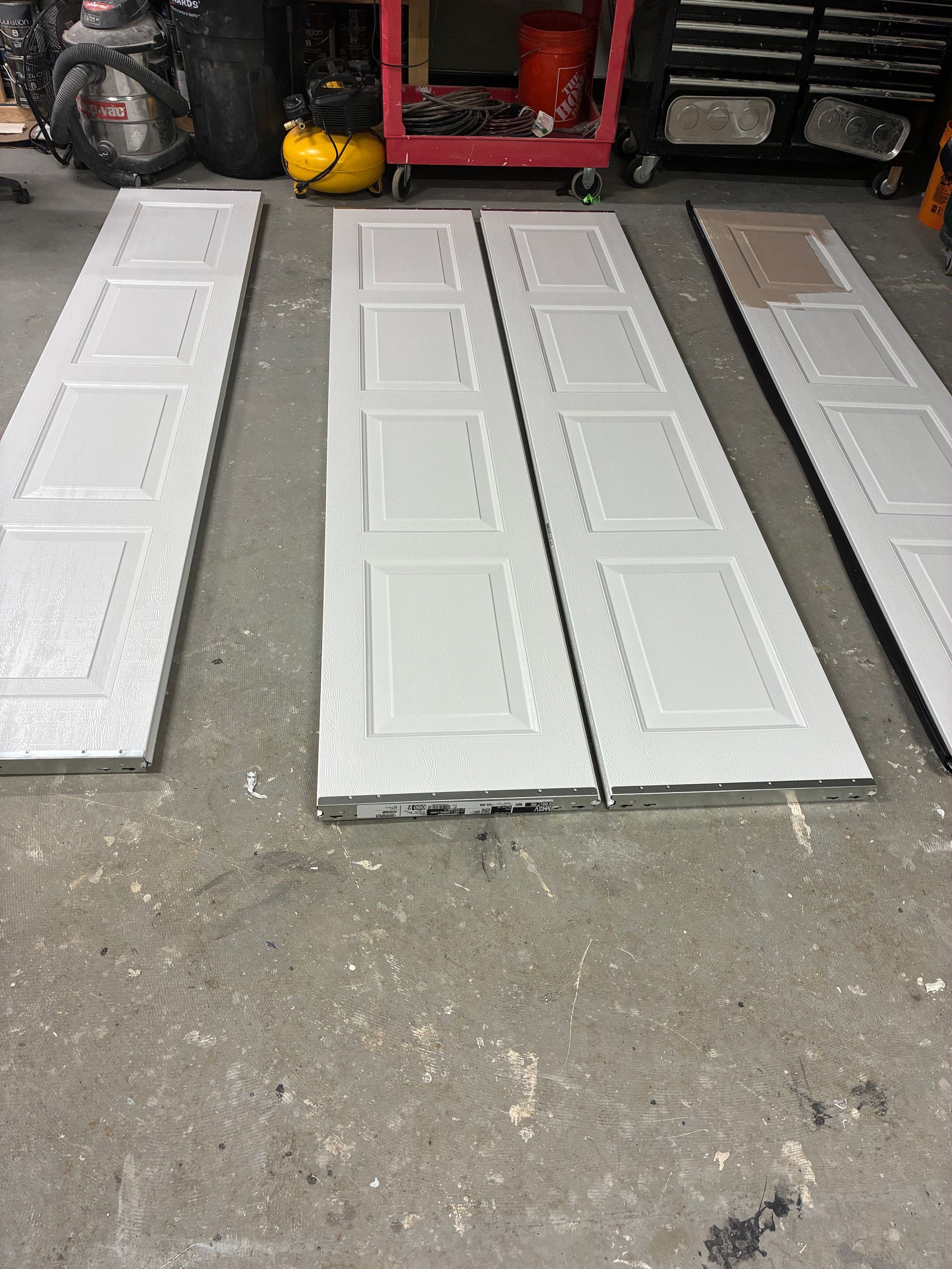 Four white paneled garage doors laid flat on a concrete floor in a workshop.