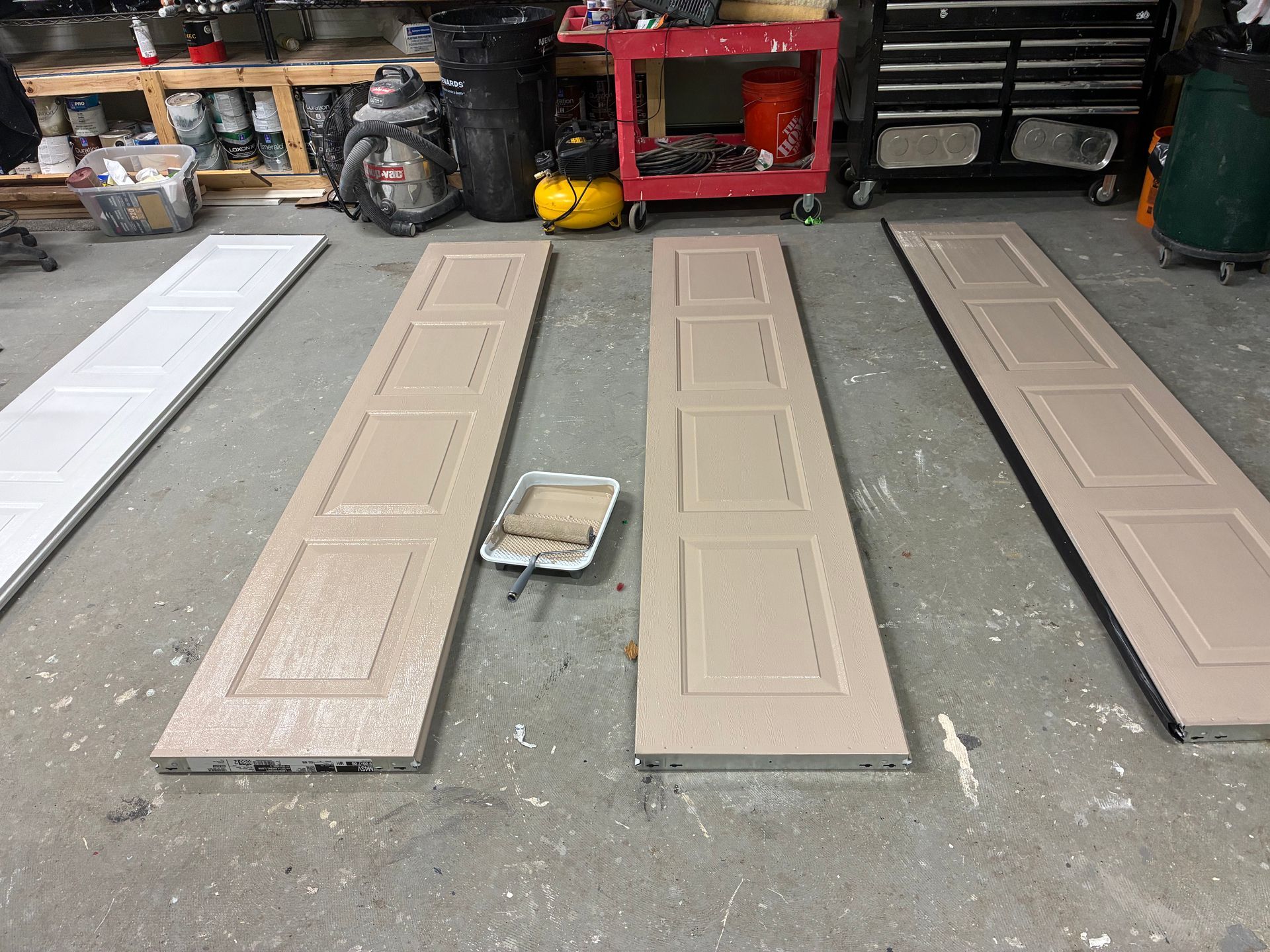 Four long tan panels laid on a garage floor, with a paint tray and workshop tools in the background.
