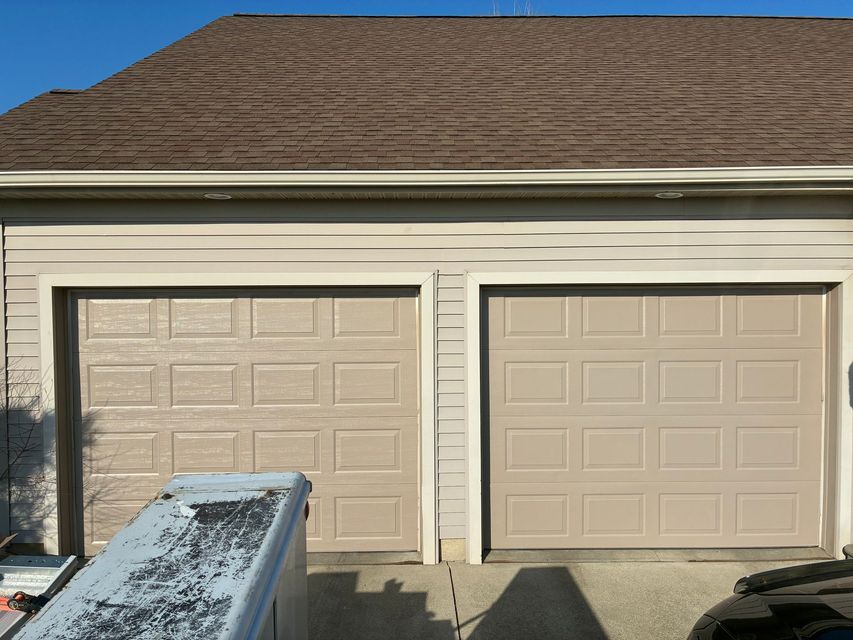 Two beige garage doors on a house with a snow-covered car hood in the foreground