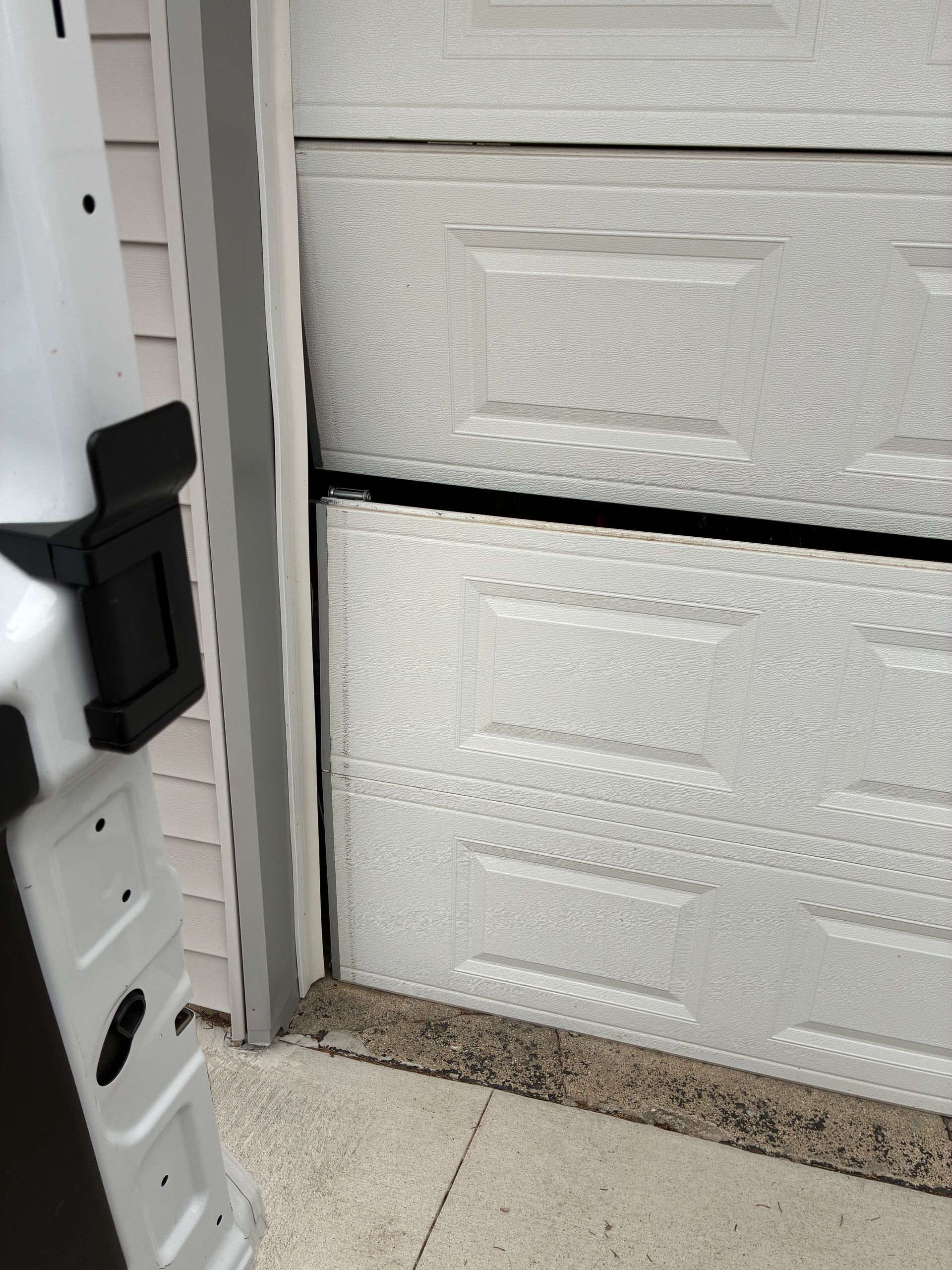 White garage door partially open with a black door latch and concrete floor in the foreground