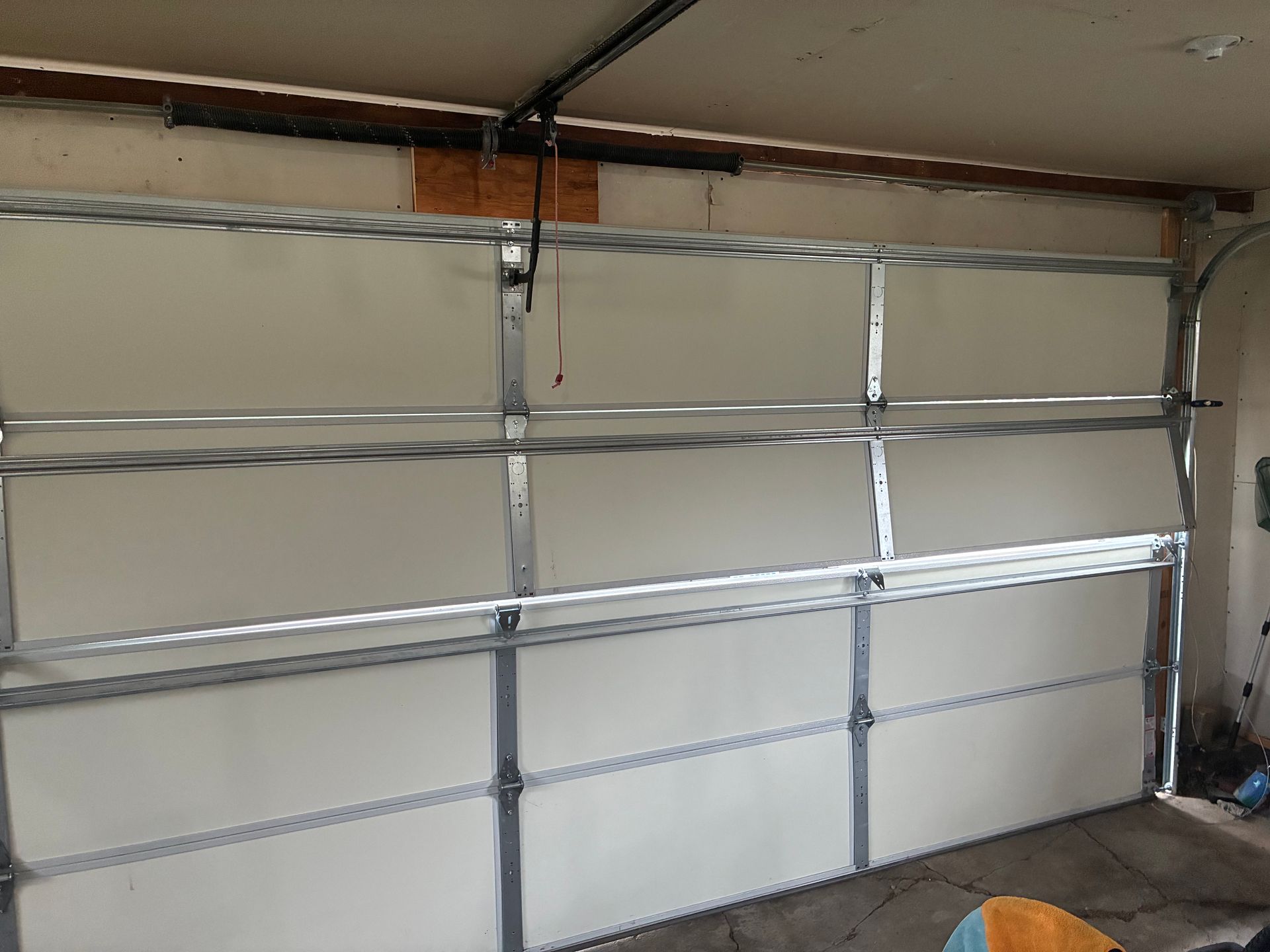Closed white garage door with metal panels and windows, viewed inside a garage.