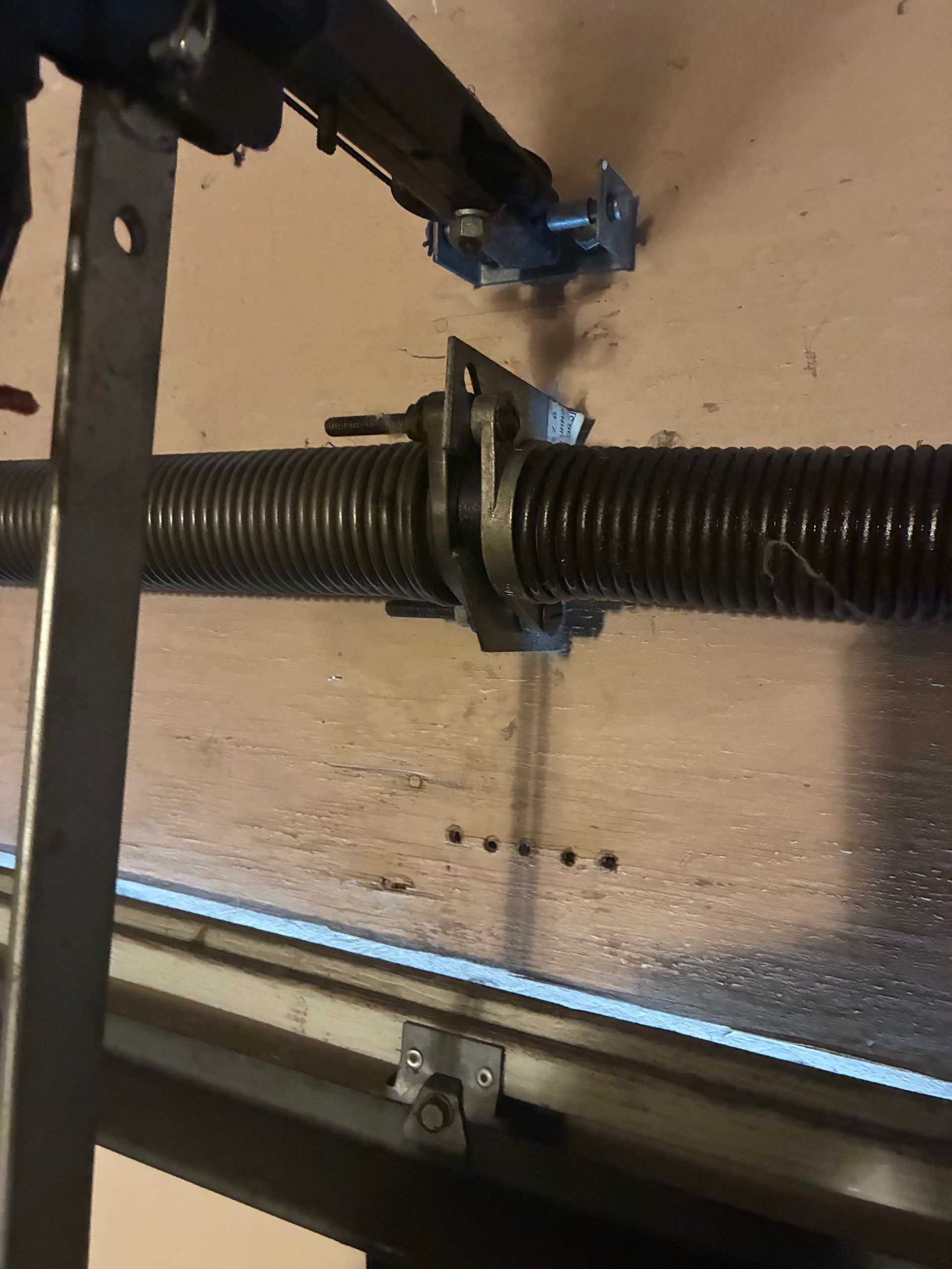 Close-up of a black threaded rod with a metal clamp and hinge mounted on a beige wall panel.