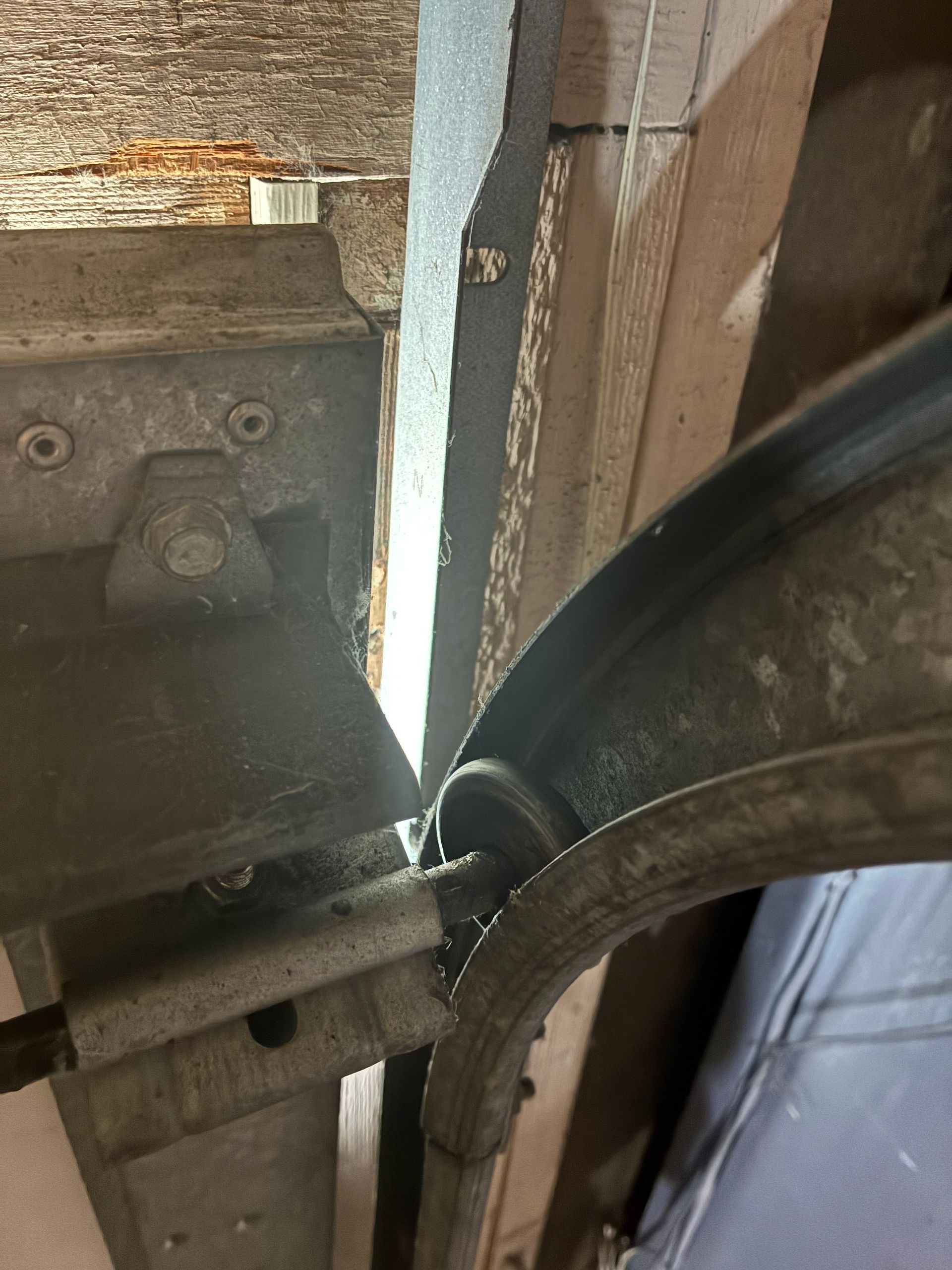 Close-up of a metal hinge and black cable beside a weathered wooden structure.