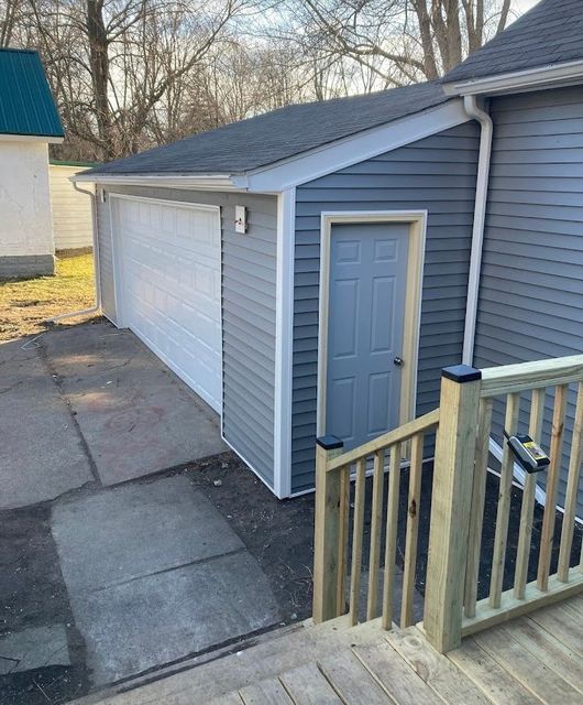 Detached garage with white doors, blue siding, and a side entry door beside a wooden railing