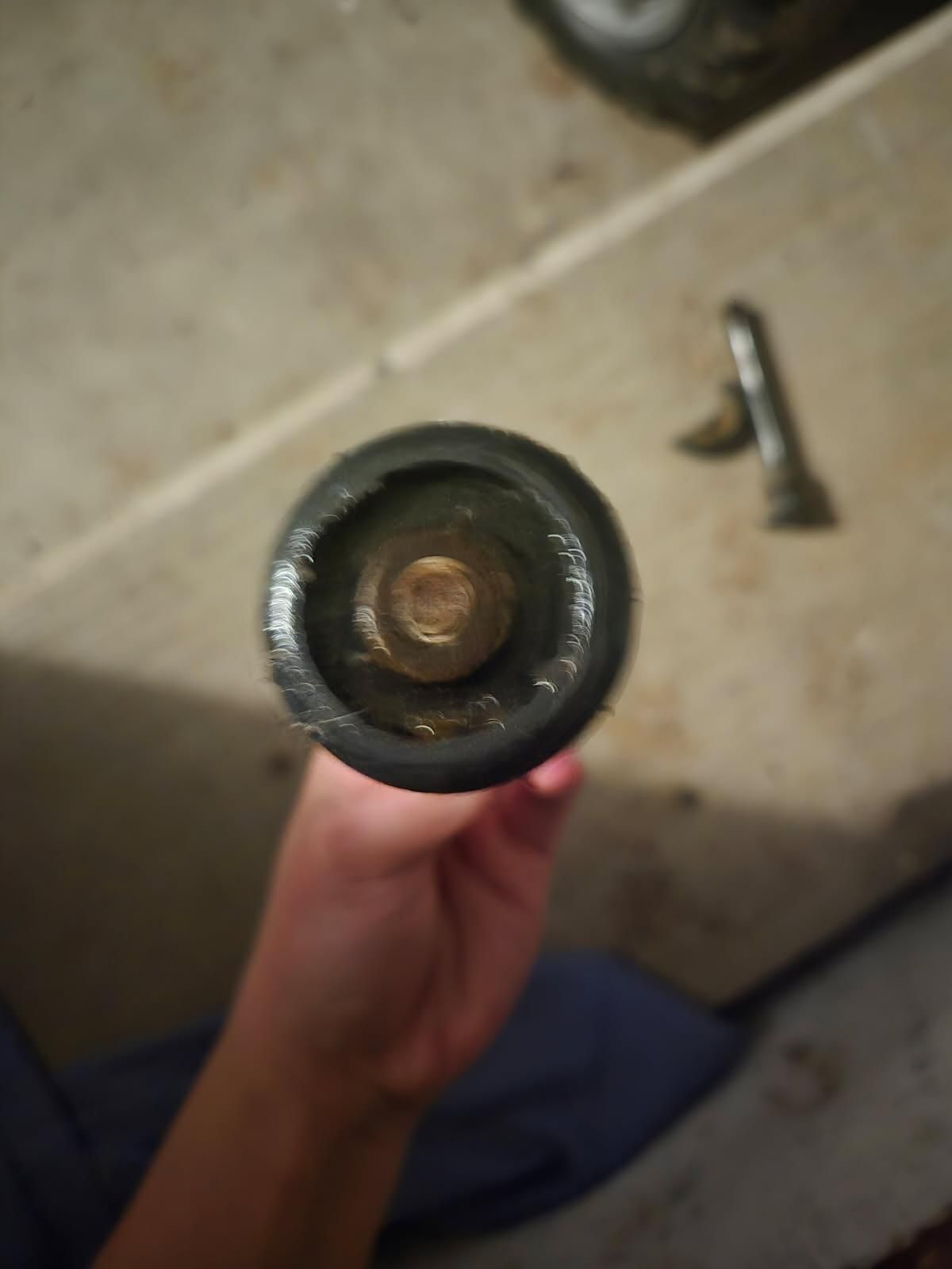 Close-up of a hand holding a black flashlight, with a beige floor and a small tool in the background.