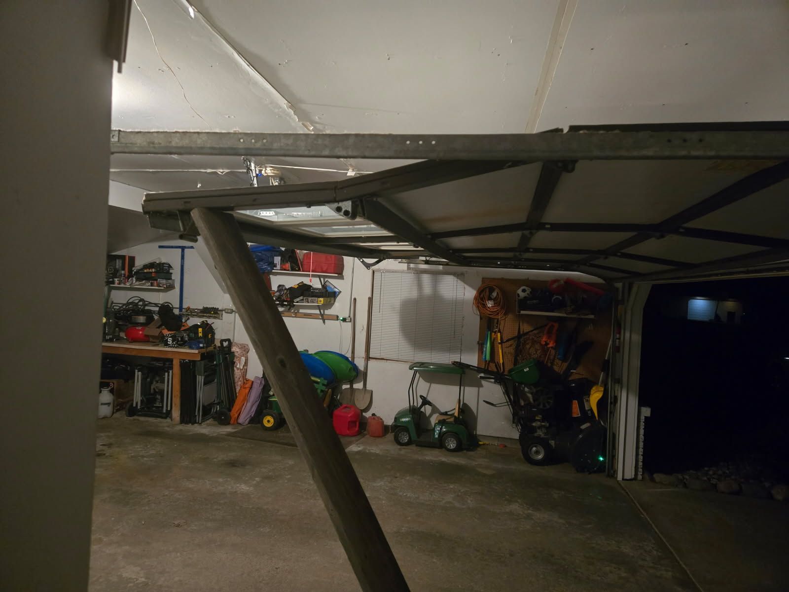 Garage interior with a metal support beam, shelves, tools, and lawn equipment near an open doorway