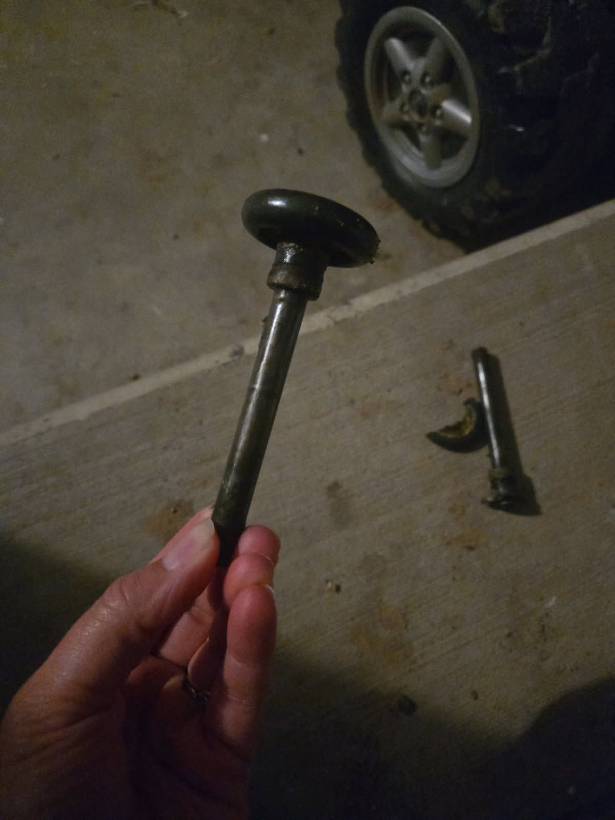 Hand holding a metal rod with a black knob in a garage; car tire visible in the background