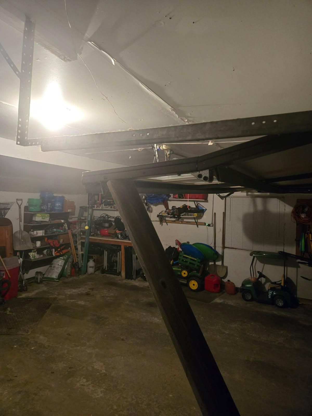 Collapsed ceiling in a garage, with debris and a support beam leaning across the floor.