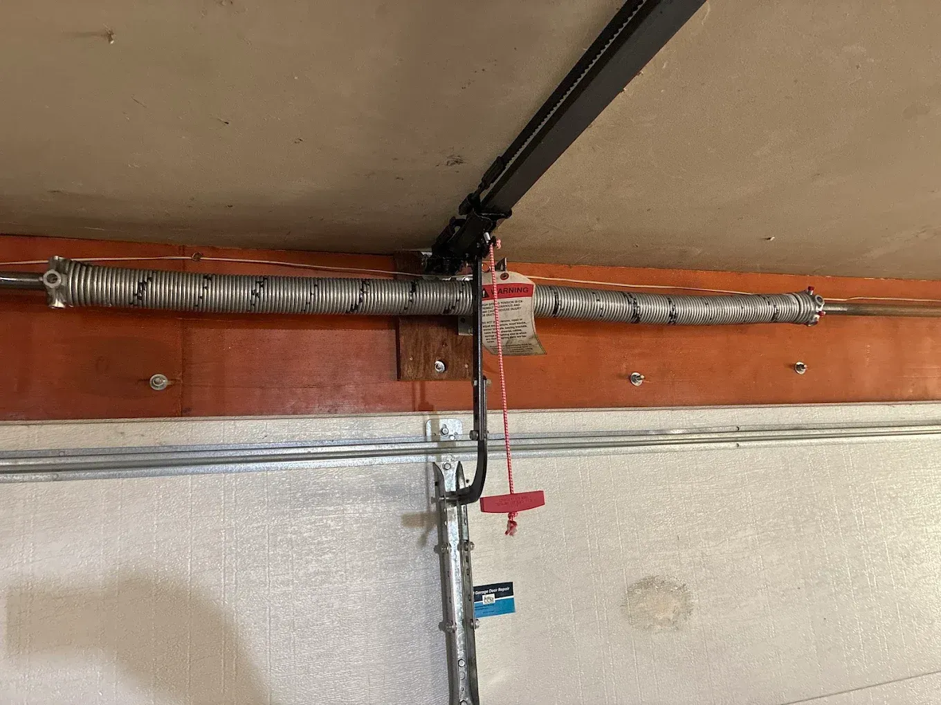 Garage ceiling with a hanging garage door opener rail and black cord above a white insulated wall.
