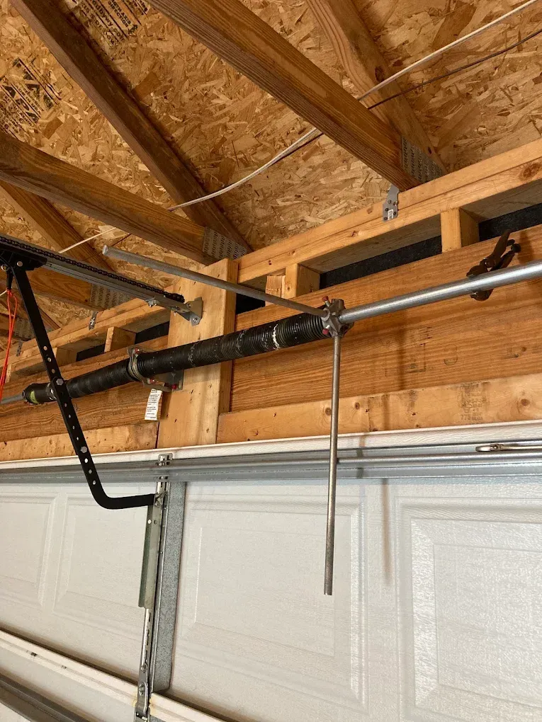 Garage ceiling with exposed rafters, a garage door opener rail, and hanging cords over a white garage door