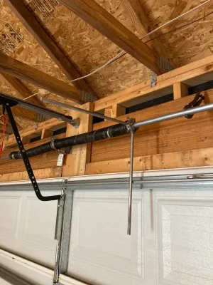 Garage ceiling with exposed rafters, a garage door opener rail, and hanging cords over a white garage door
