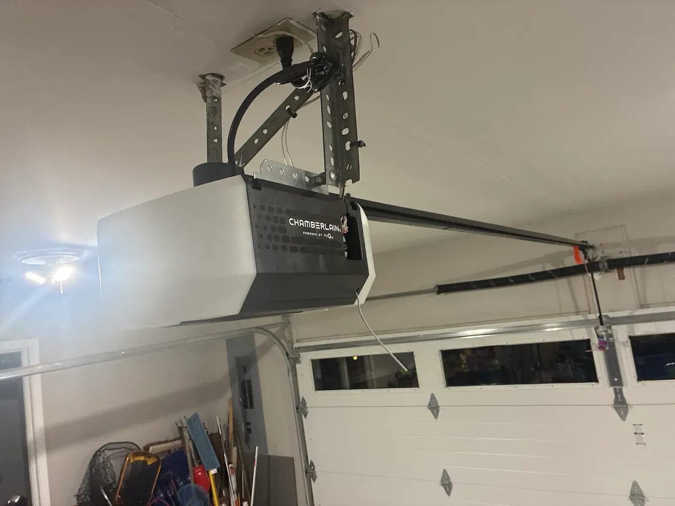 Garage door opener mounted on a ceiling with rails above a white garage door.