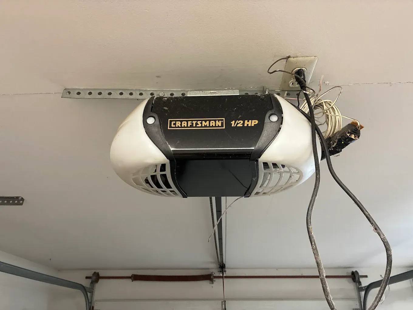 Garage door opener mounted on a ceiling with a hanging cord and exposed wiring