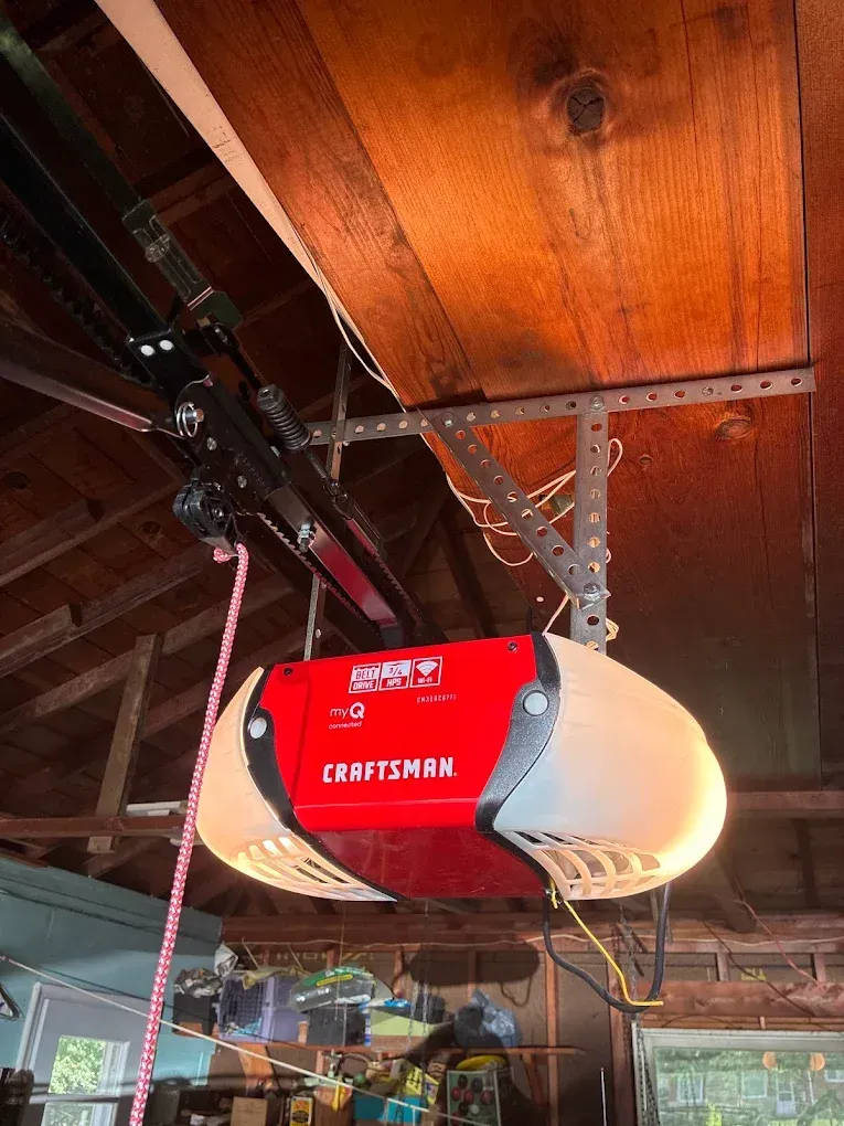 Red Craftsman garage door opener mounted on a wooden ceiling with rails and chain drive.