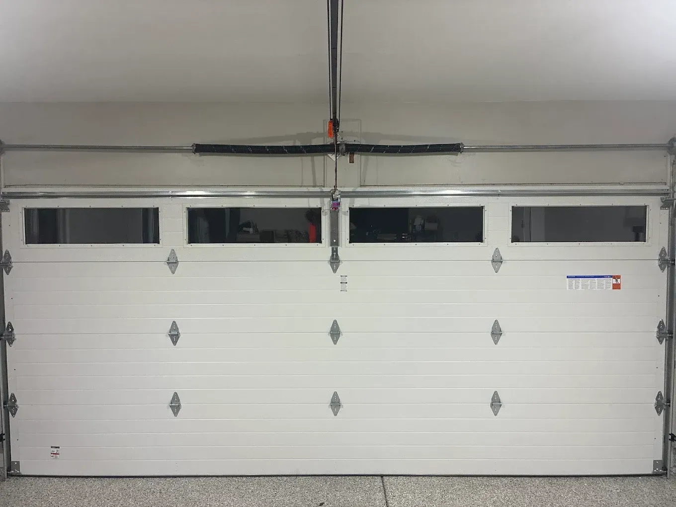 White garage door with four narrow windows and a hanging opener in a garage interior