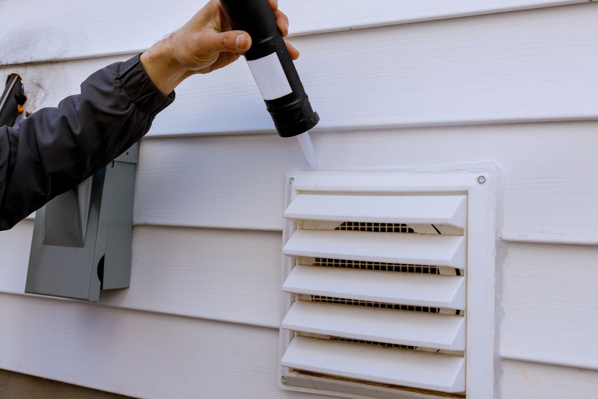Person holding a flashlight near a house exterior vent on white siding