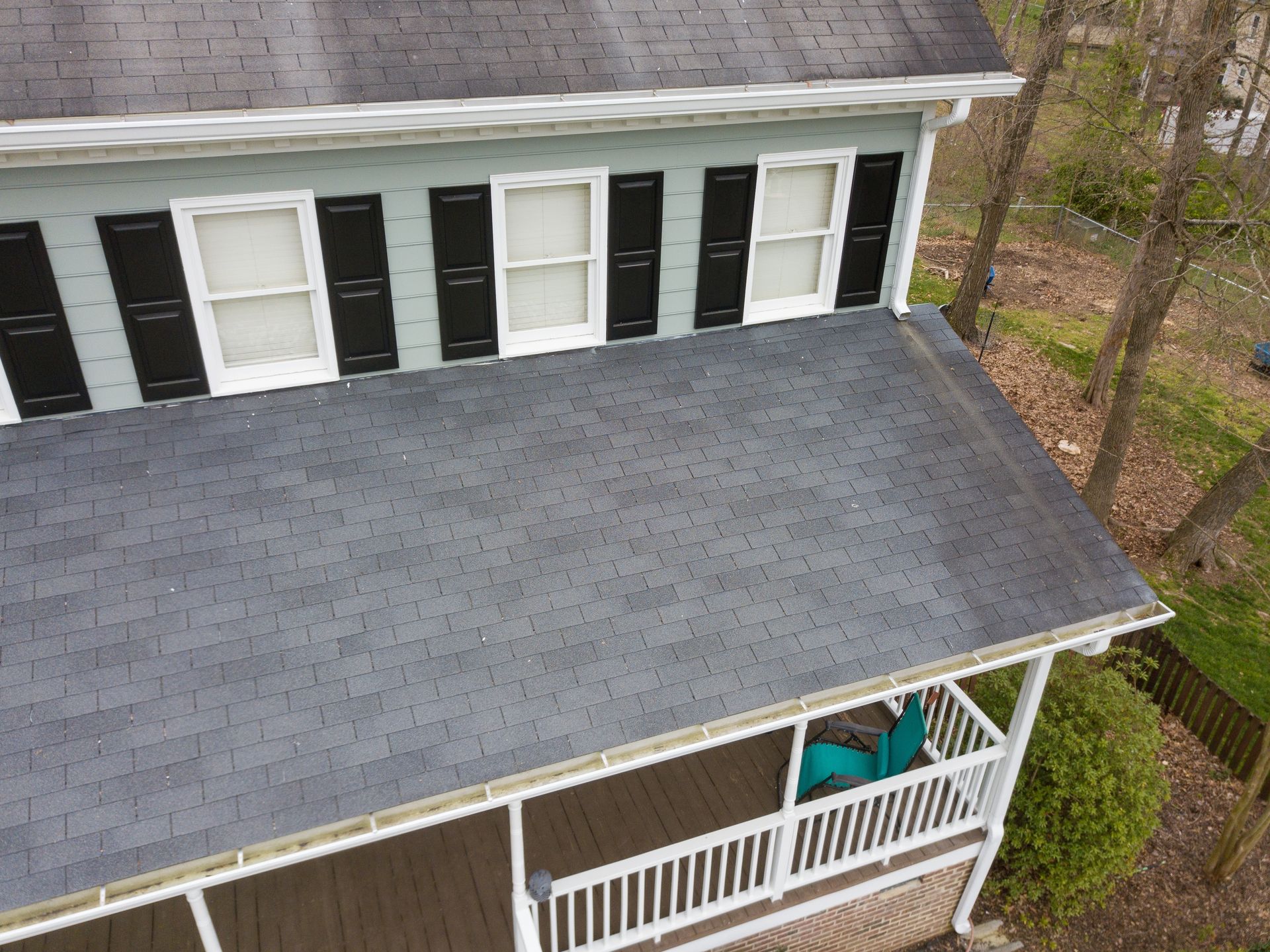 Aerial view of a gray-shingled house with black shutters and a covered front porch.