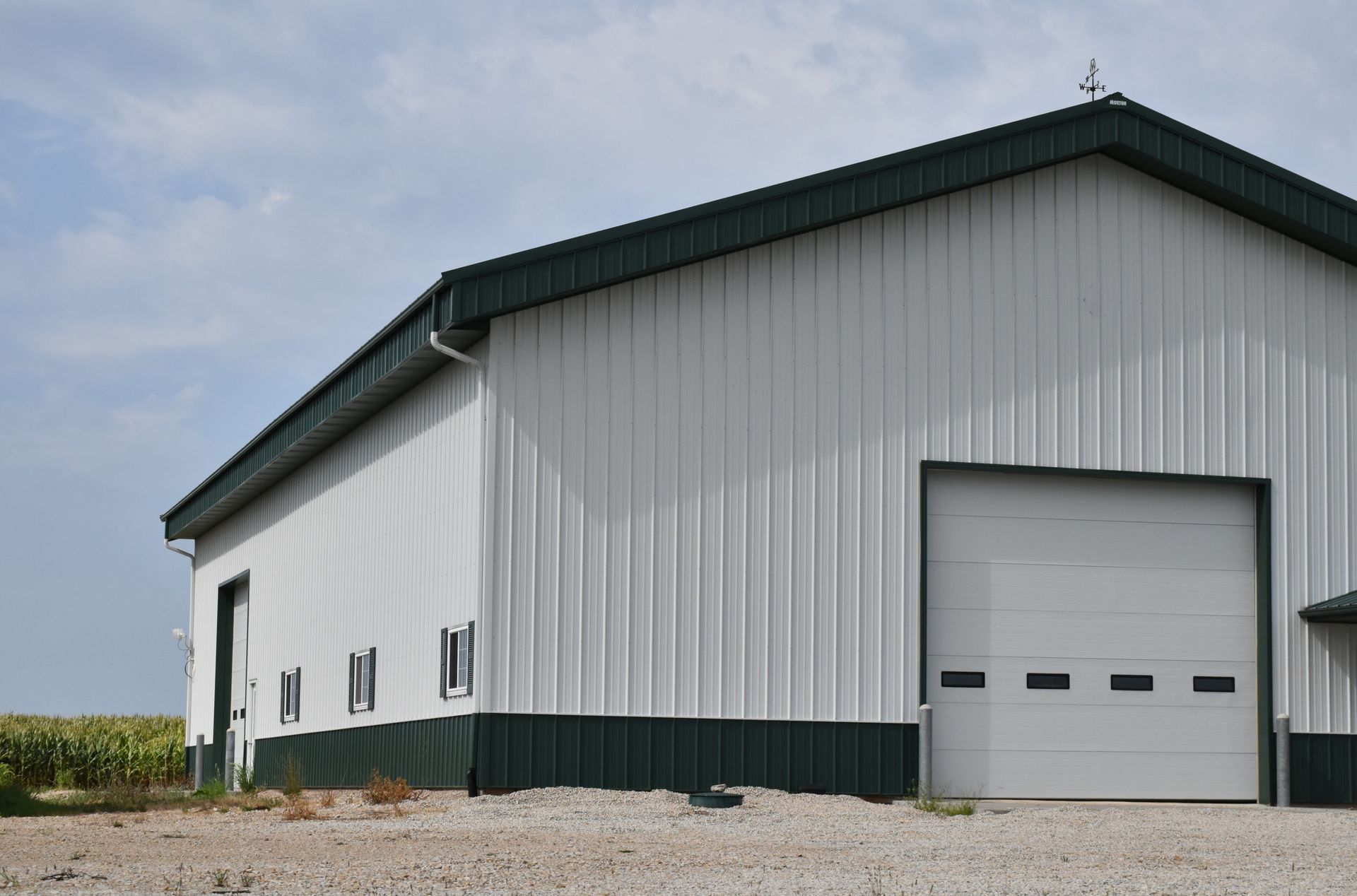 White metal barn-style building with green roof trim and a large garage door on a gravel lot