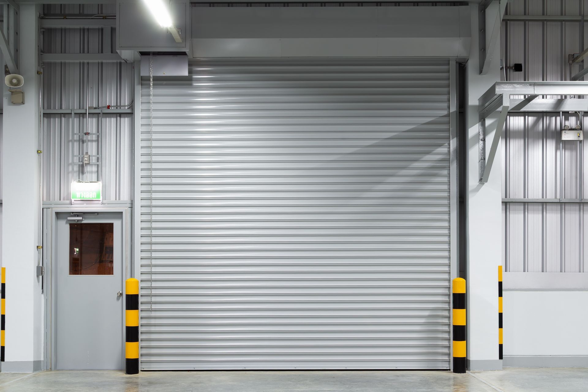 Closed gray industrial roll-up door in a warehouse with black-and-yellow safety bollards