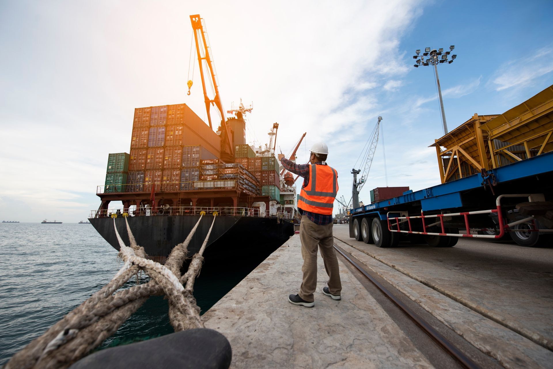 Cargo ship being loaded at a dock, with a worker in an orange vest signaling near the crane.