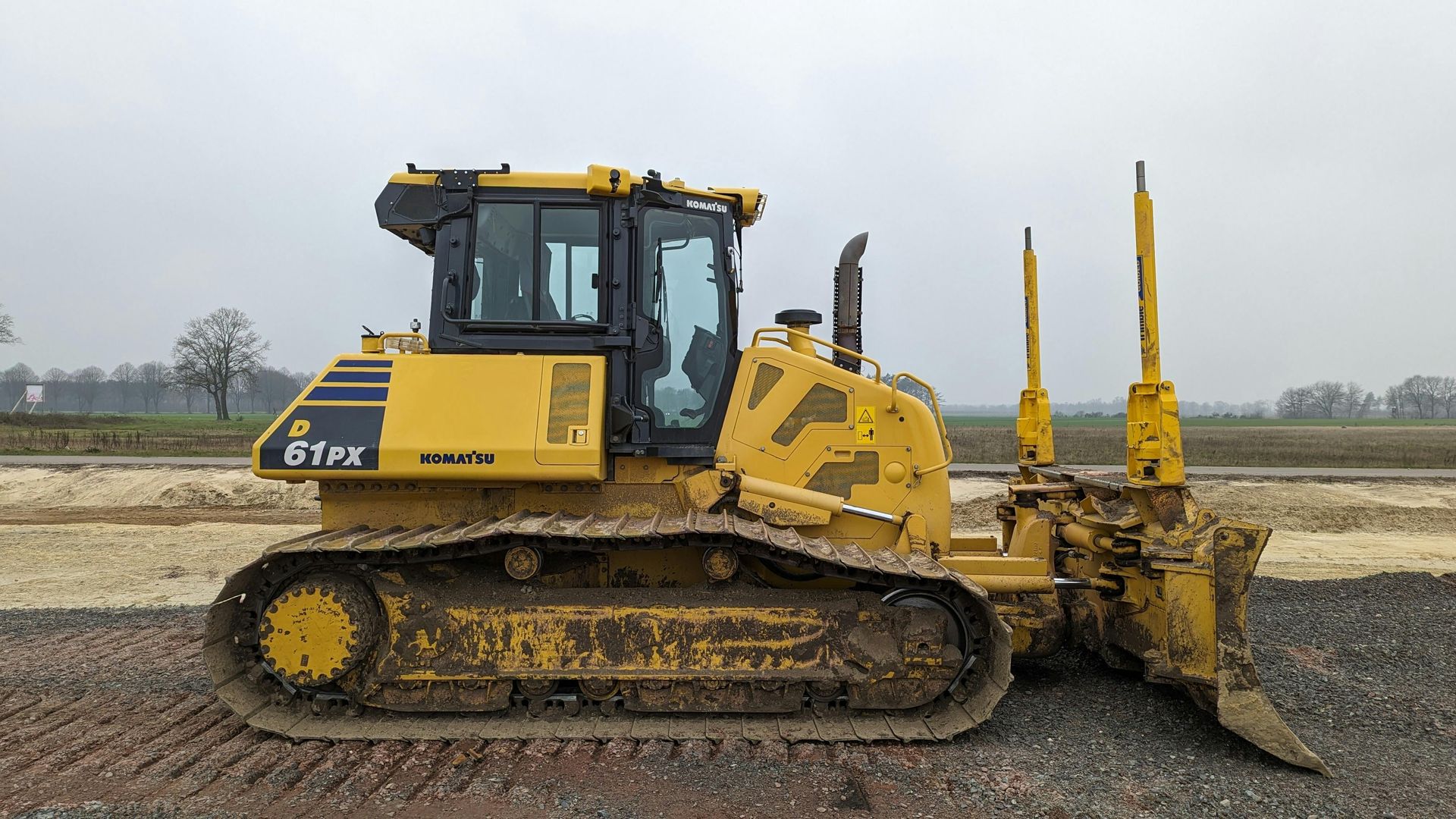 Yellow bulldozer on a construction site; it has tracks, a cab, and rippers.