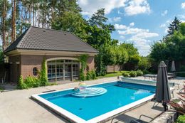 Poolside view with a rectangular pool, cabana, trees, and blue sky.